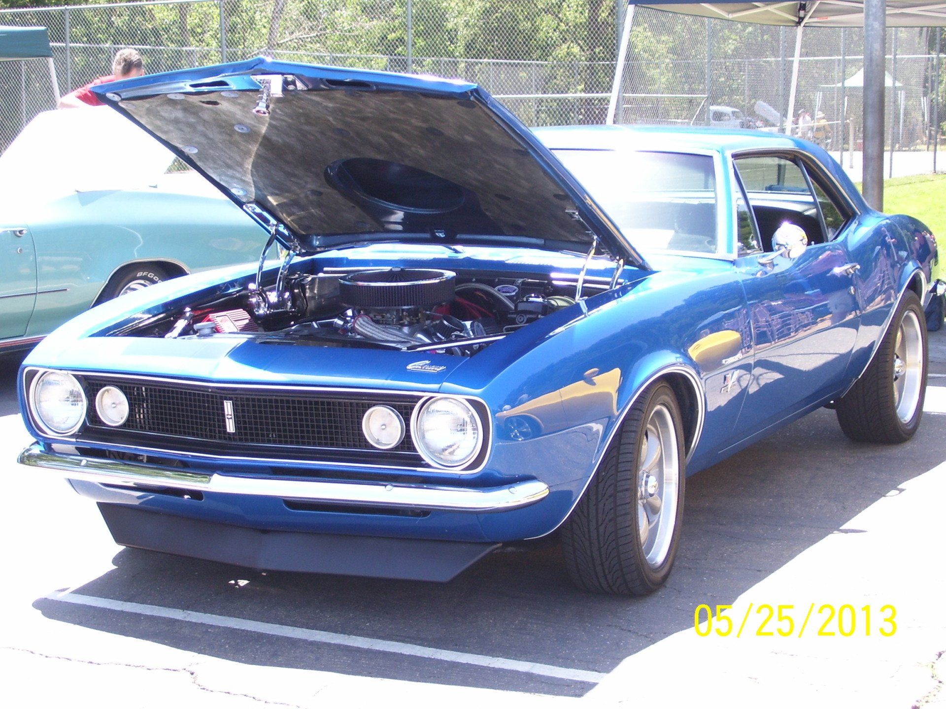 A blue car with the hood open is parked in a parking lot