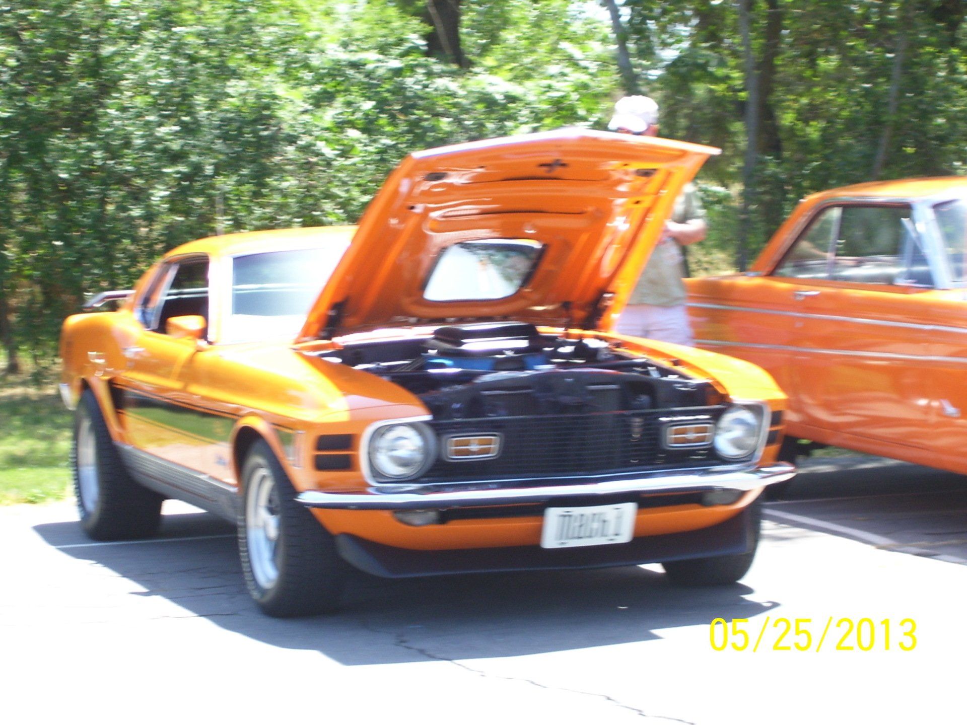 An orange car with the hood up is parked on the side of the road