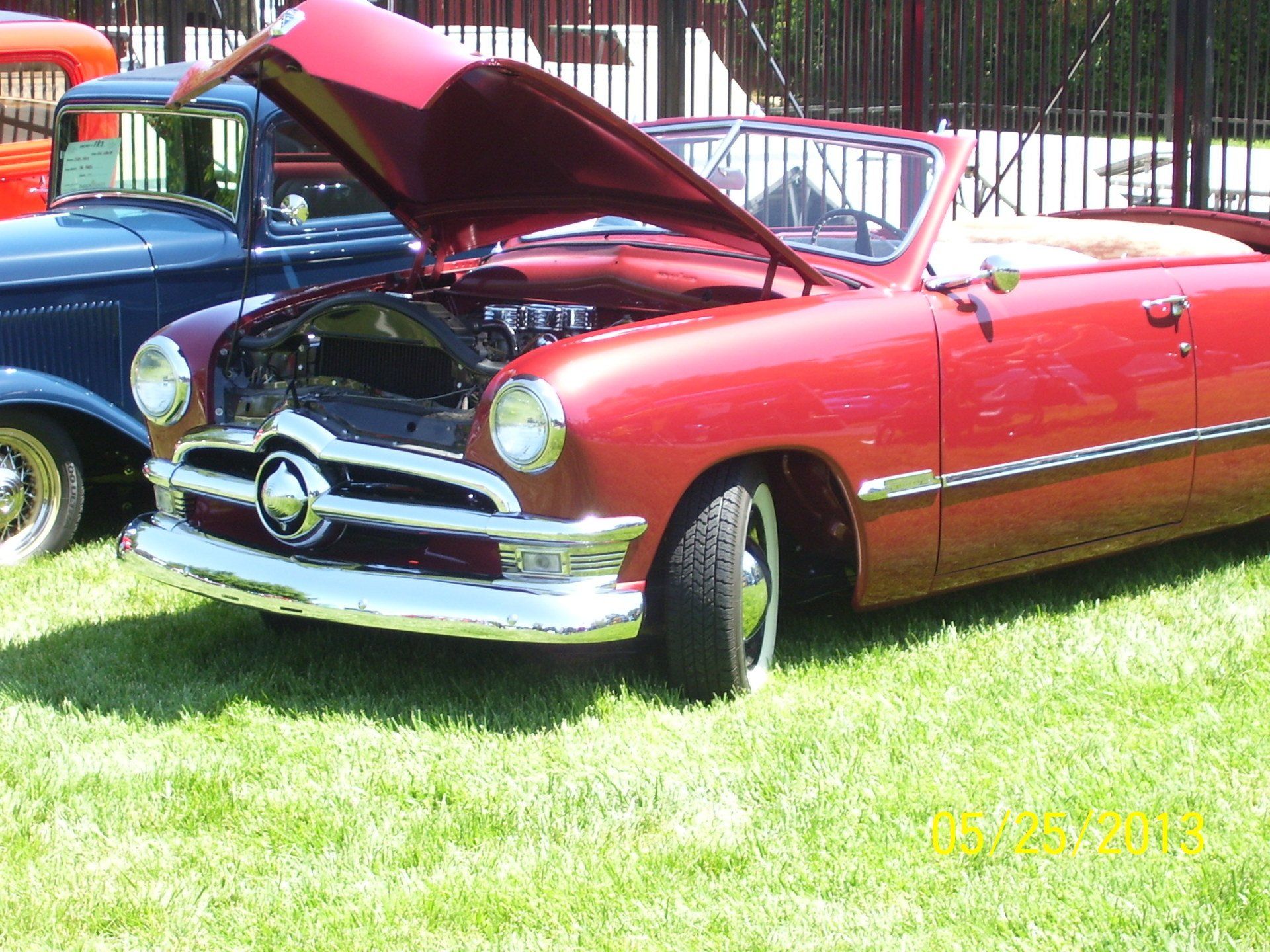 A red car with the hood up is parked in the grass