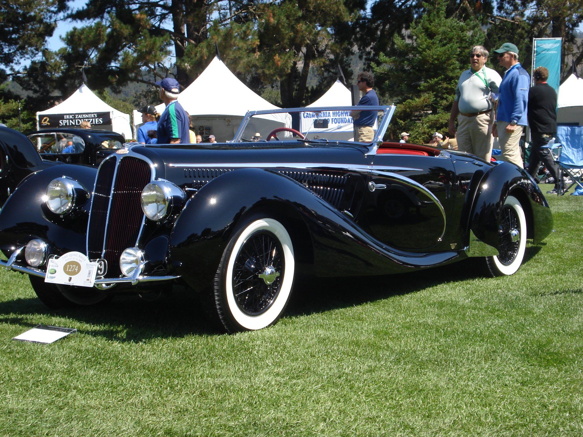 A black car with white tires is parked in the grass