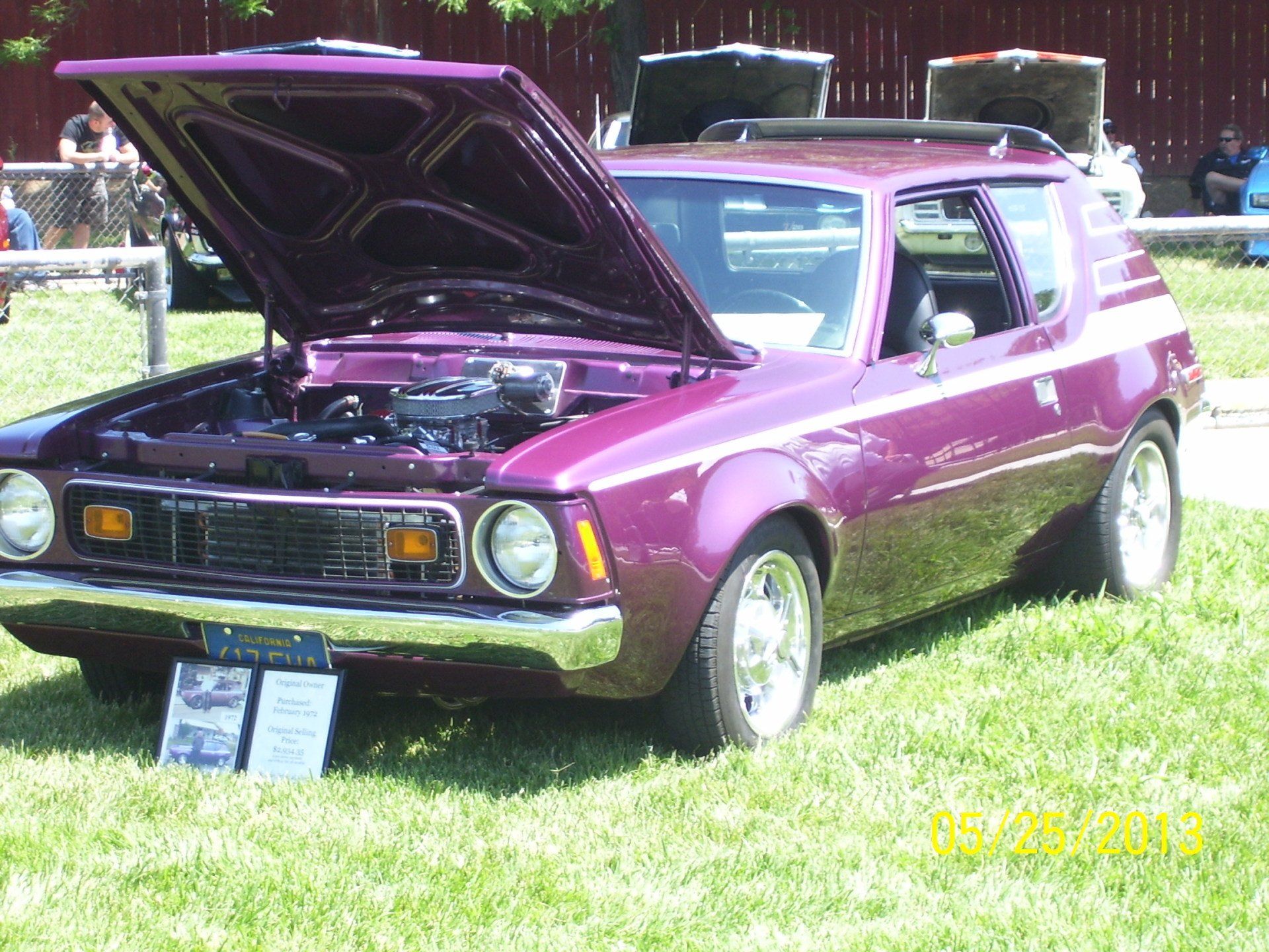 A purple car with the hood up is parked in the grass