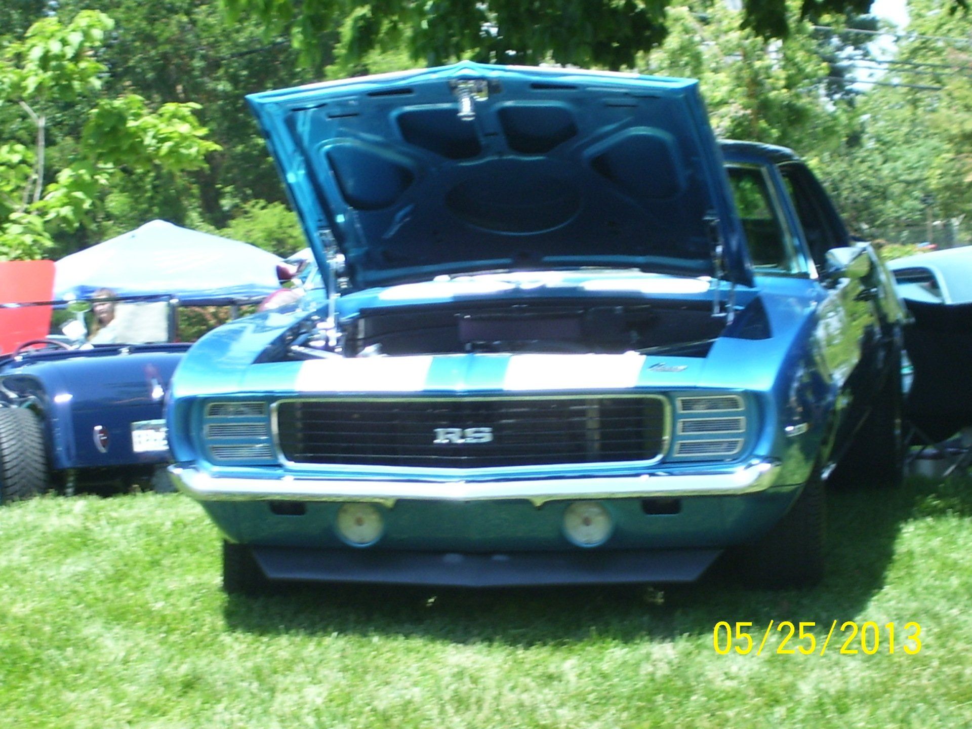 A blue car with the hood up is parked in the grass