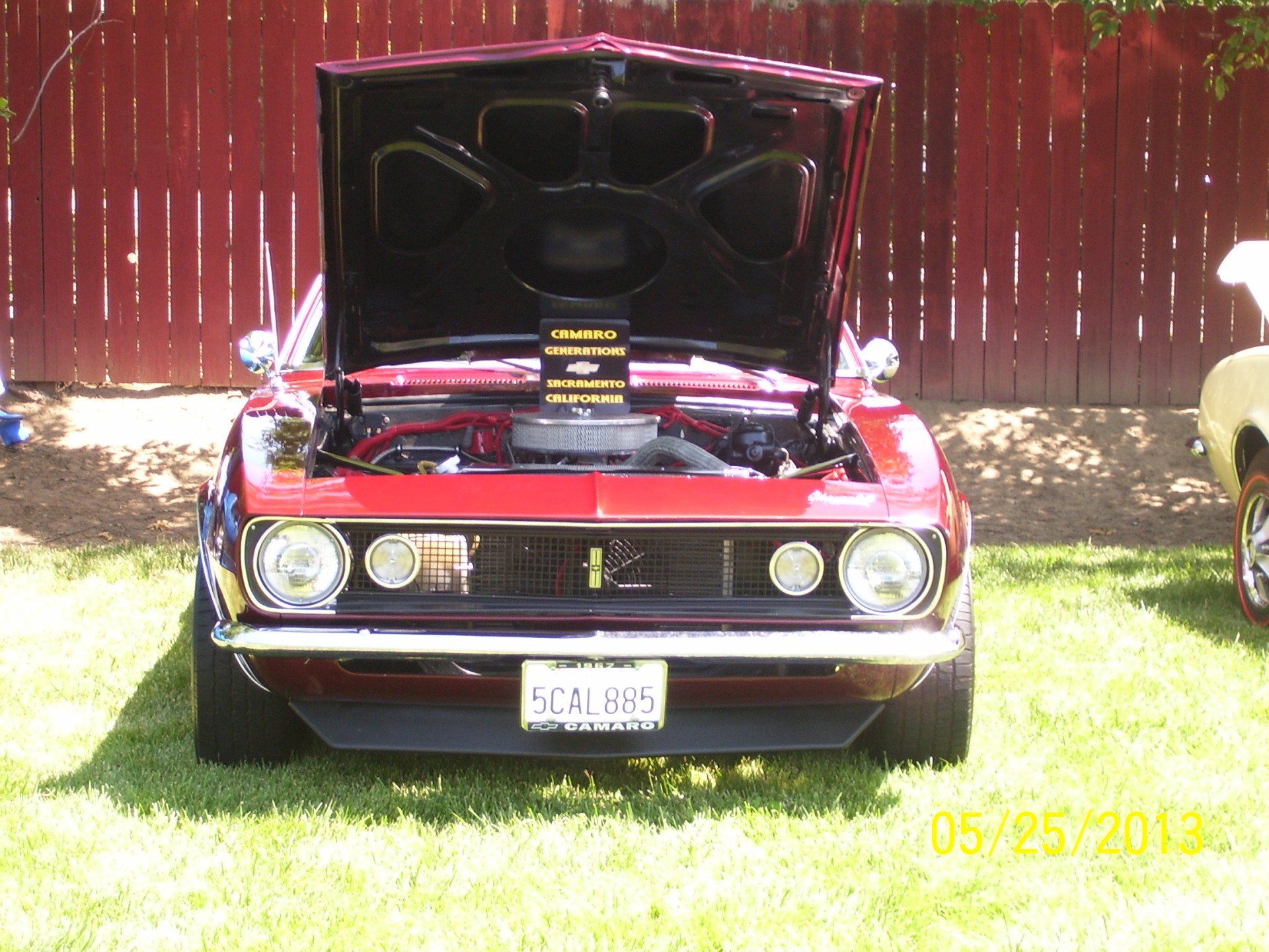 A red car with the hood up is parked in the grass