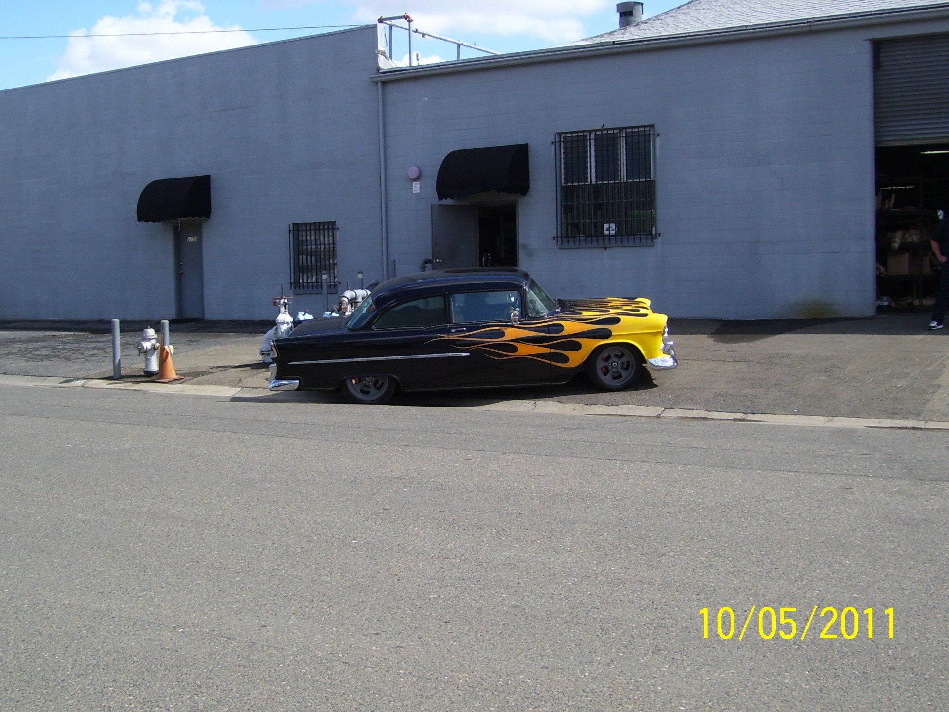 A black and yellow car with flames painted on it is parked in front of a building