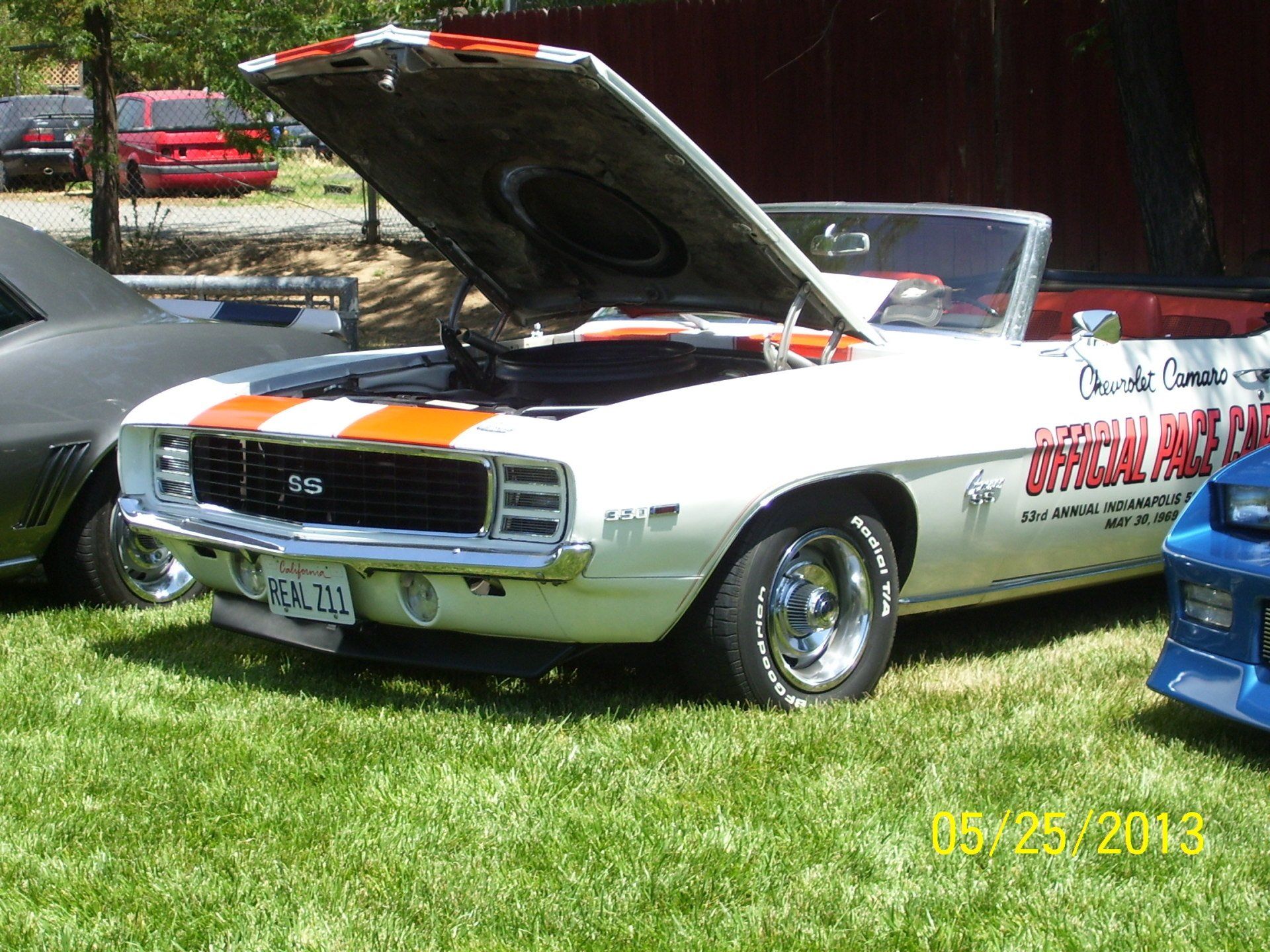A white car with the hood up is parked in the grass