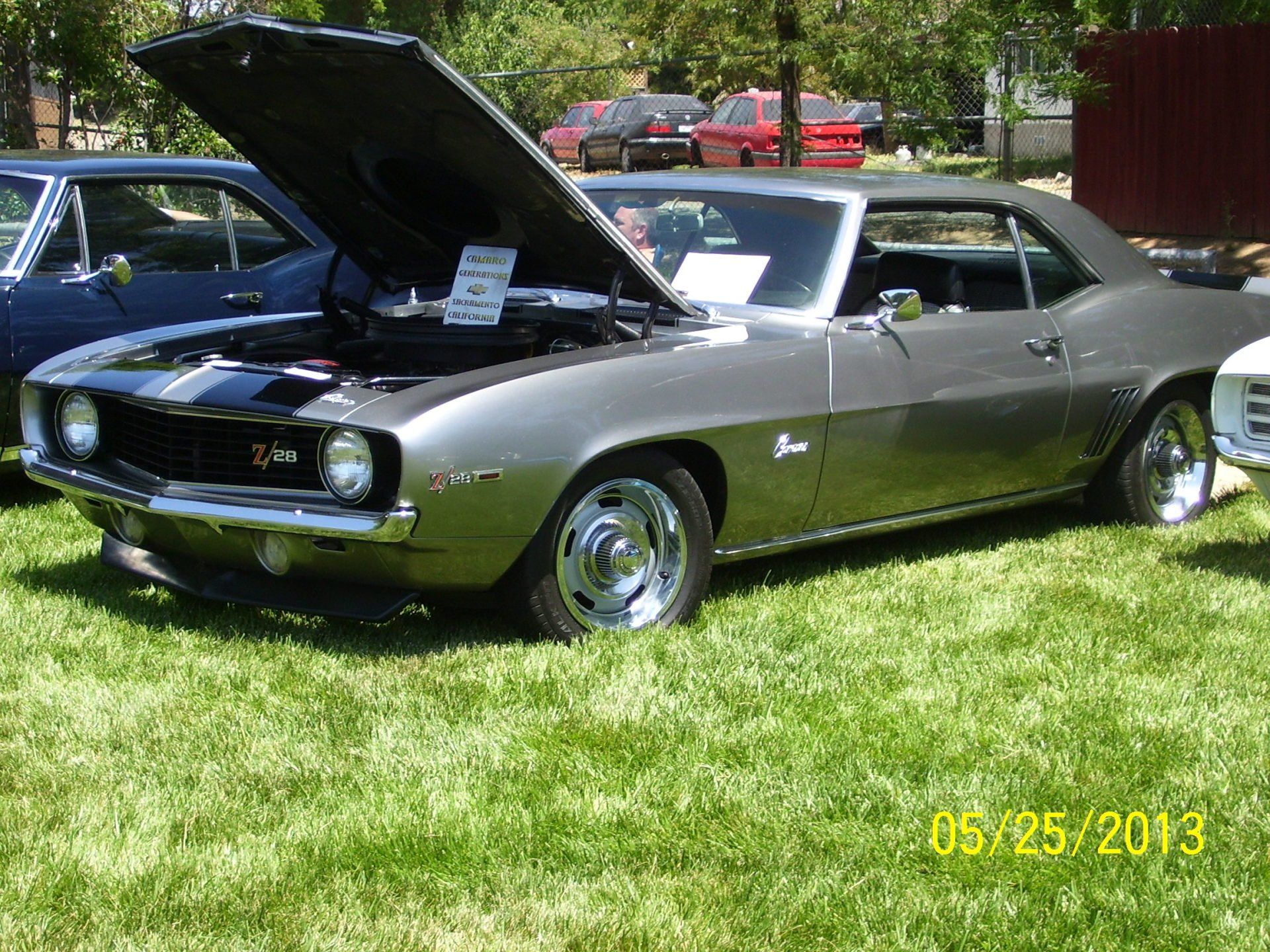 A silver car with the hood up is parked in the grass