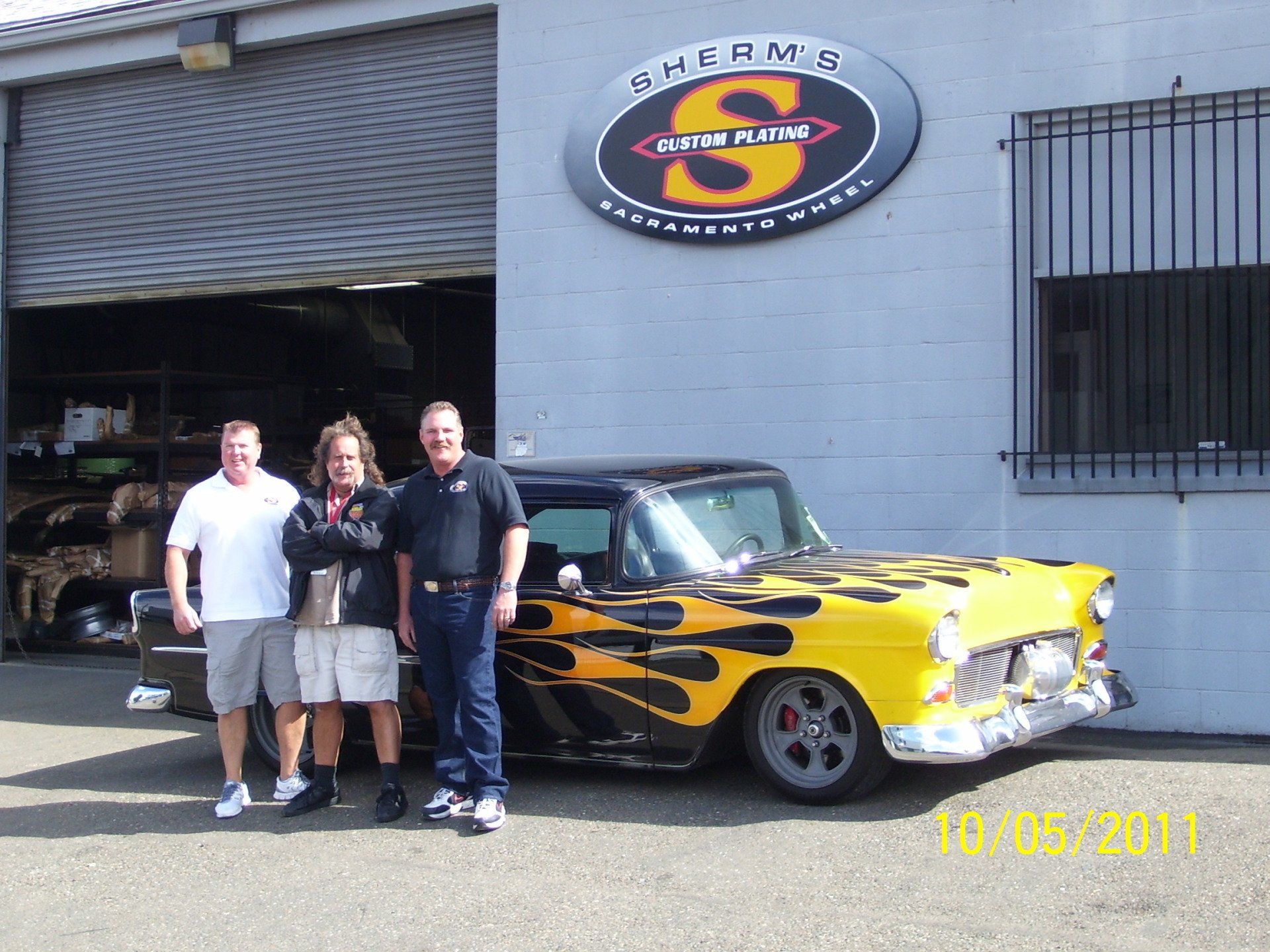A group of men standing in front of a yellow car with flames painted on it