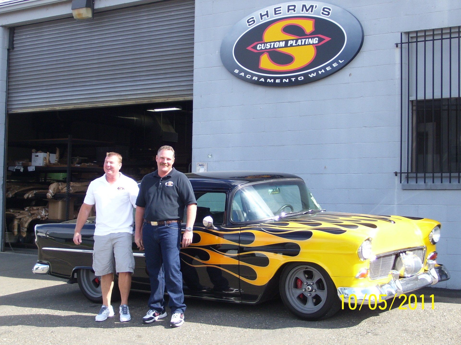 Two men standing in front of a yellow car with flames painted on it