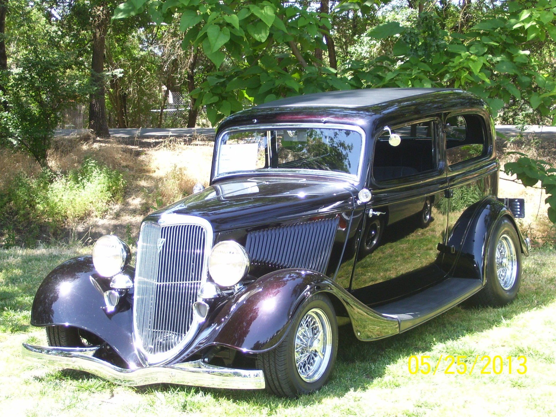 A black car is parked in the grass under a tree