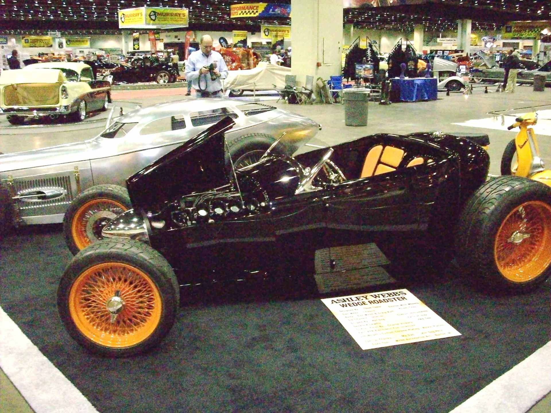 A black car with orange wheels is on display at a car show