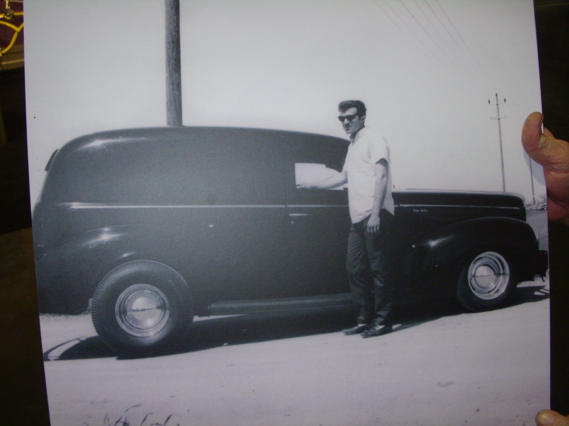 A black and white photo of a man standing next to a black car