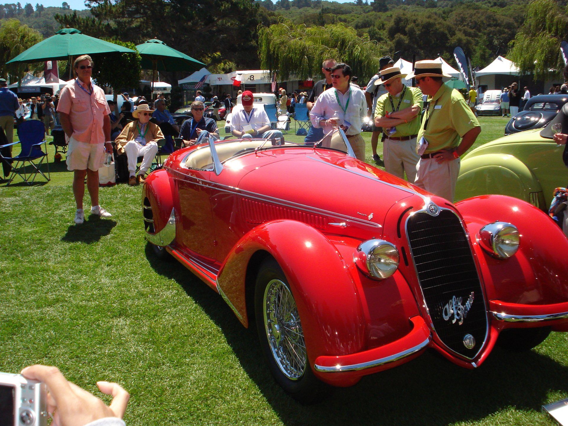 A man is taking a picture of a red car at a car show