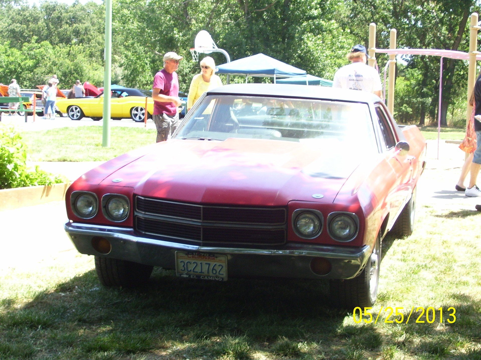 A red car is parked in a grassy area with people standing around it