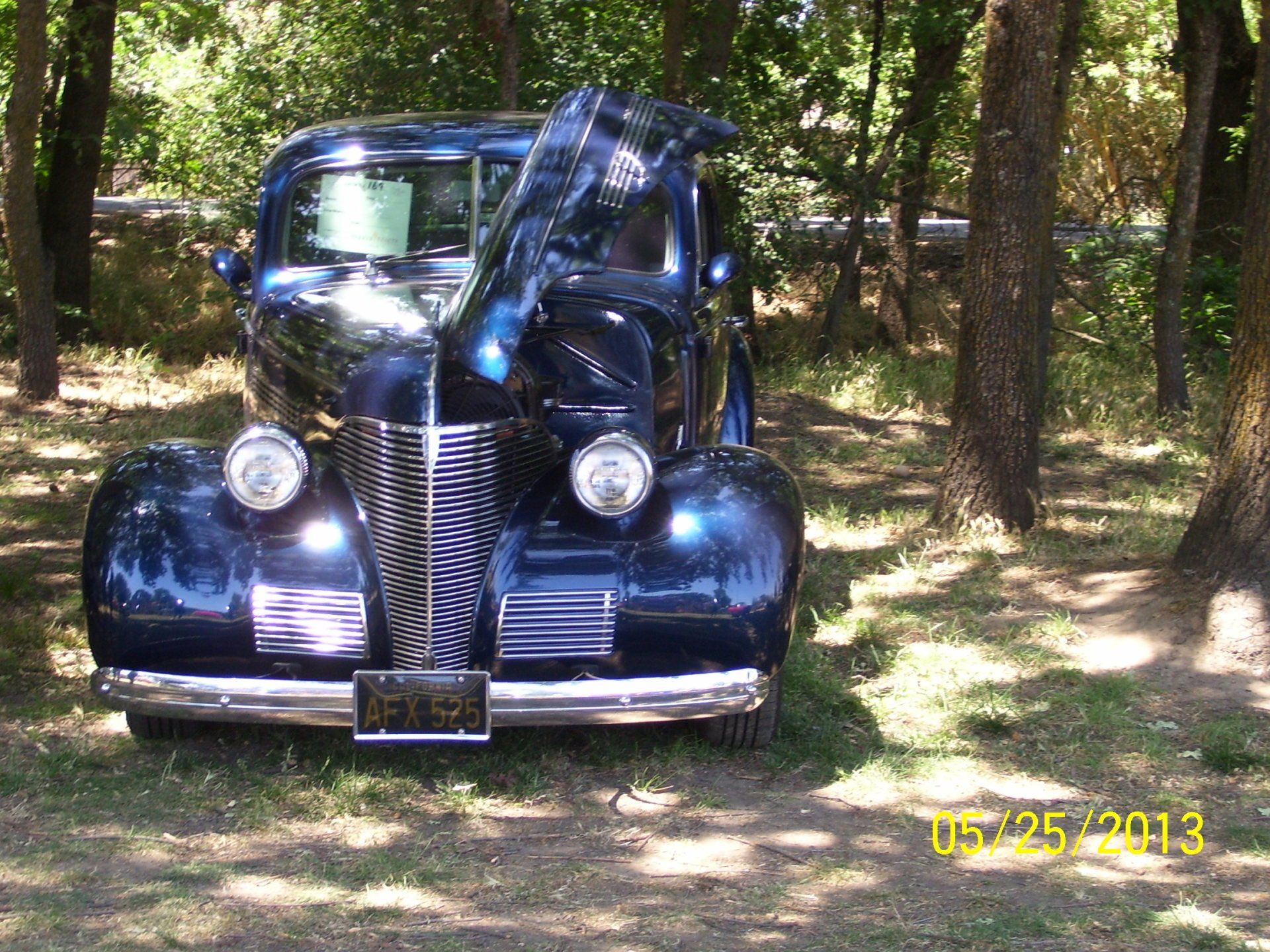 A black car is parked in the woods with the hood up