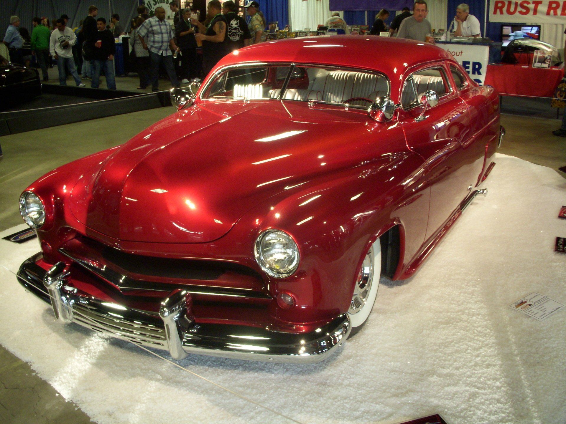 A red car is on display in front of a rust repair sign