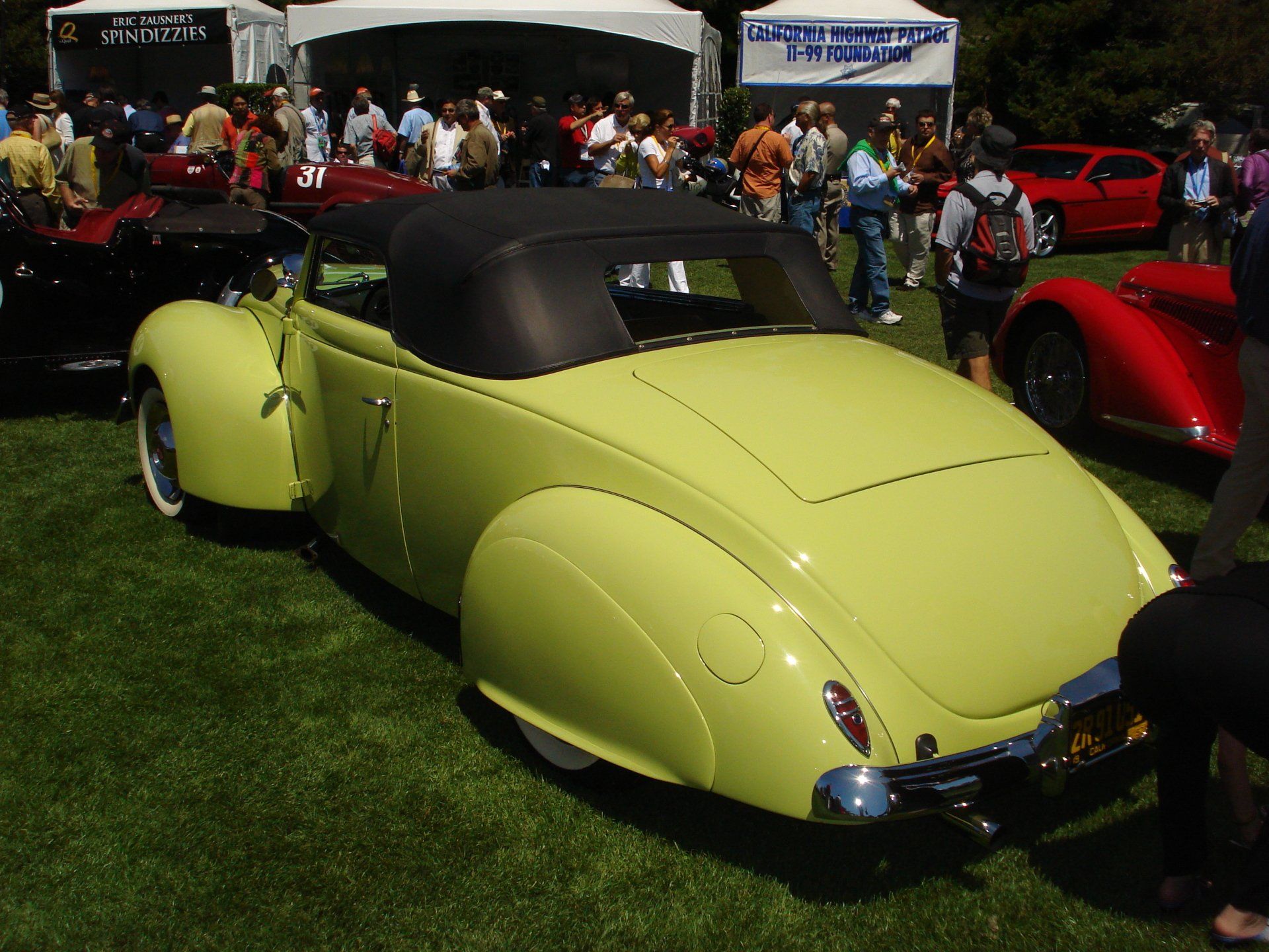 A yellow car is parked in the grass at a car show