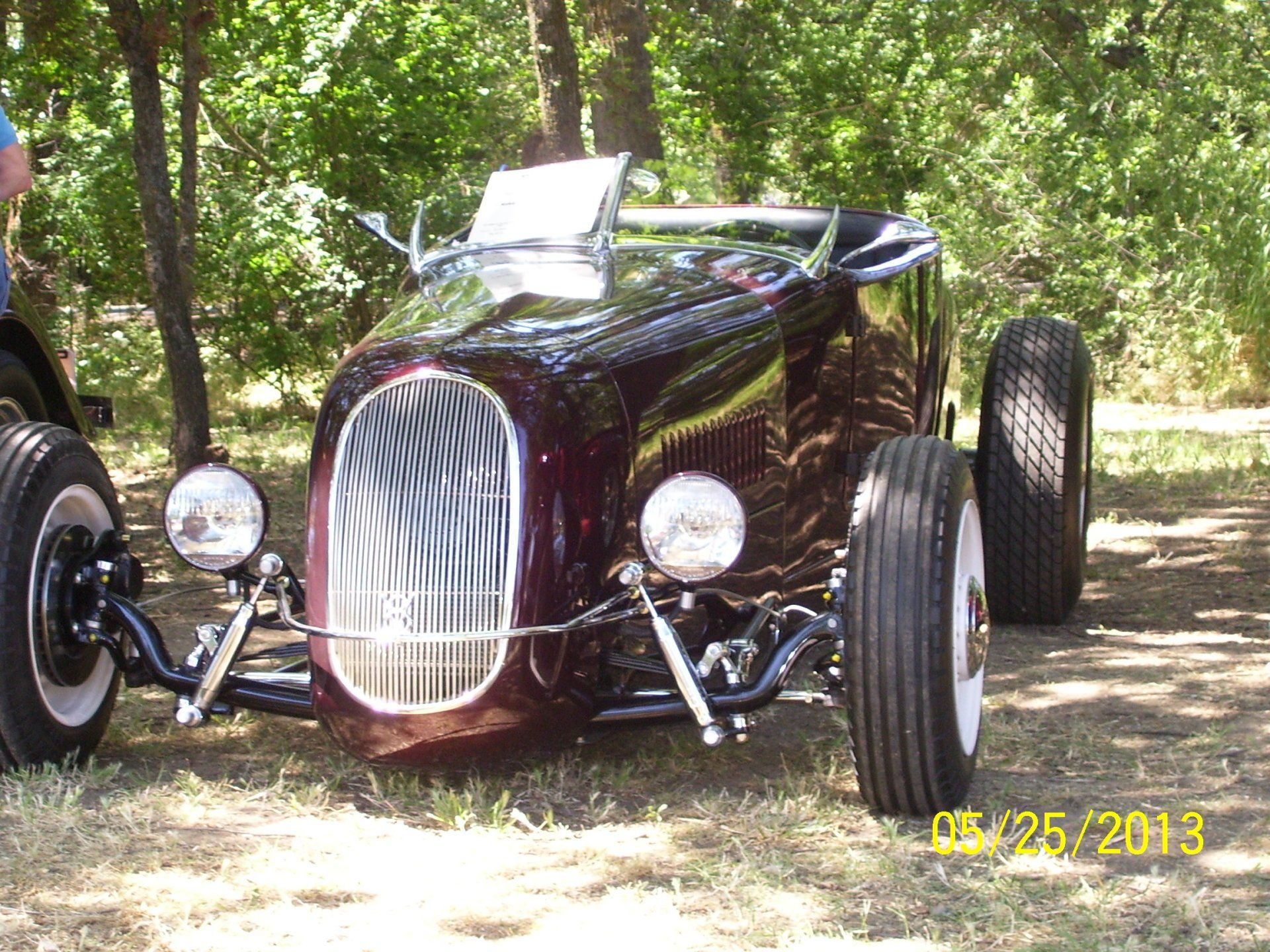 A black hot rod is parked in the grass with trees in the background