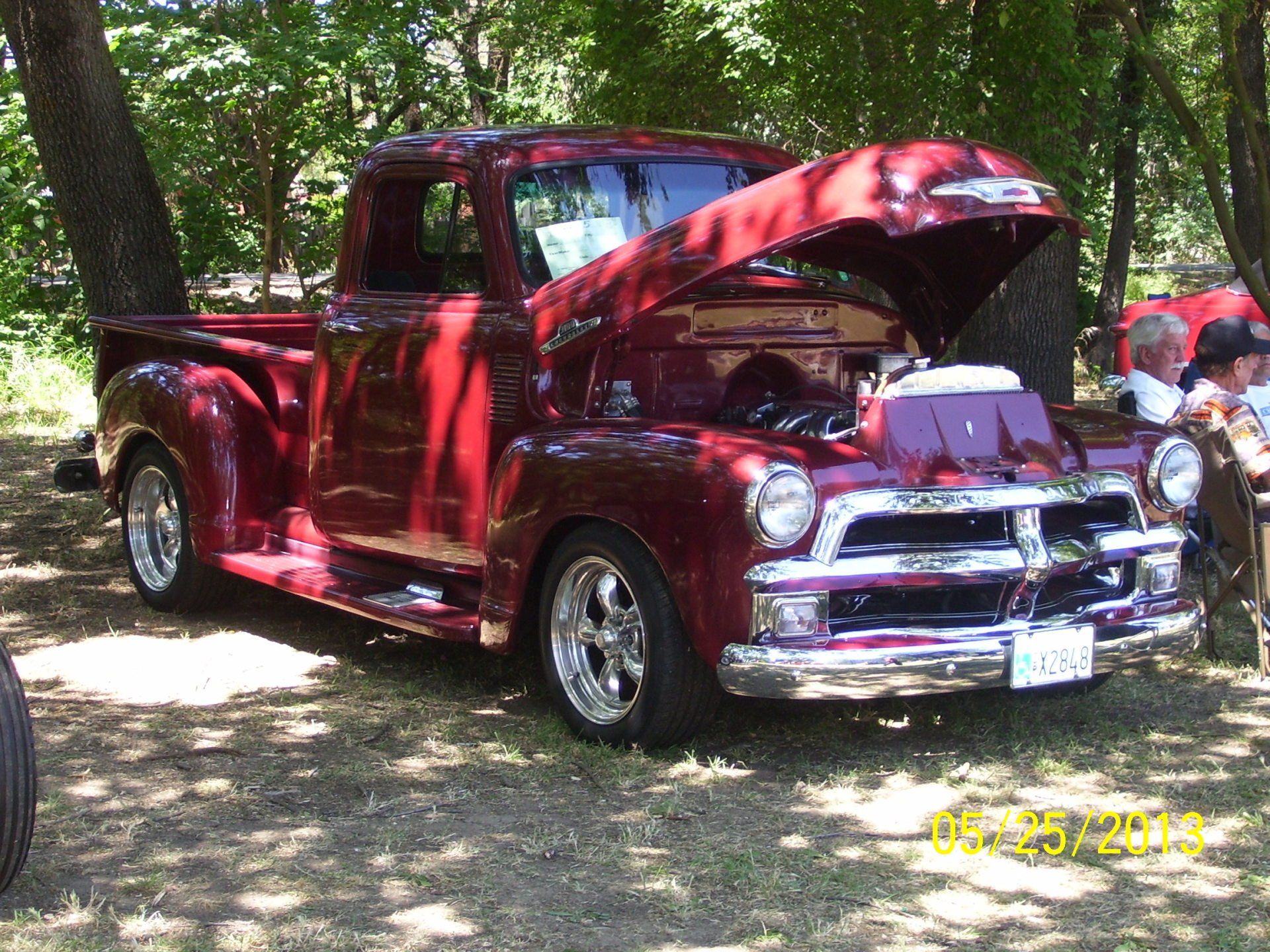 A red truck with the hood up is parked in the woods