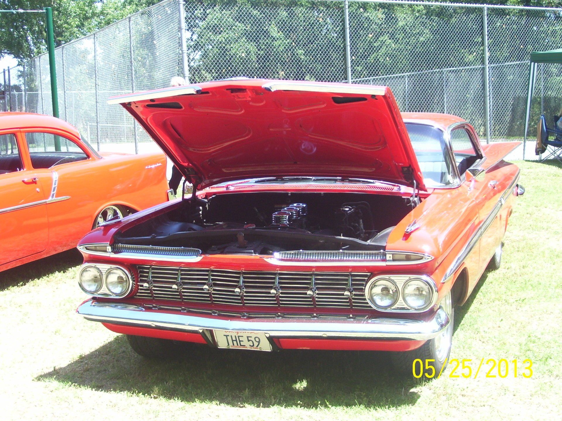 A red car with the hood up is parked in the grass