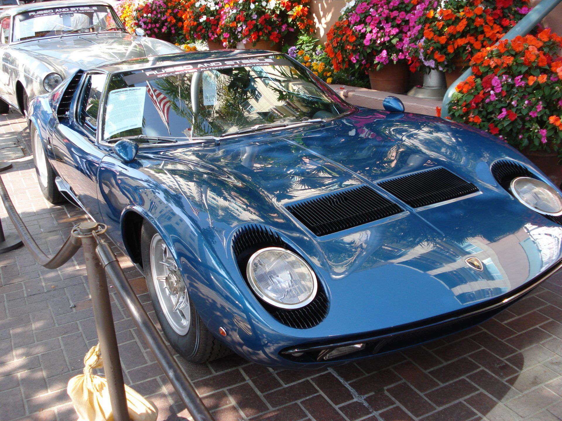 A blue sports car is parked in front of flowers