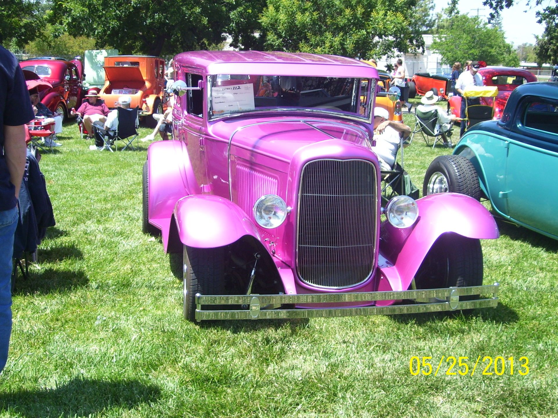 A pink car is parked in the grass at a car show
