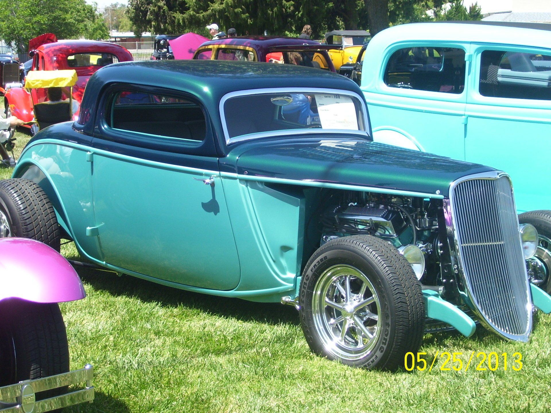 A blue car is parked in the grass at a car show