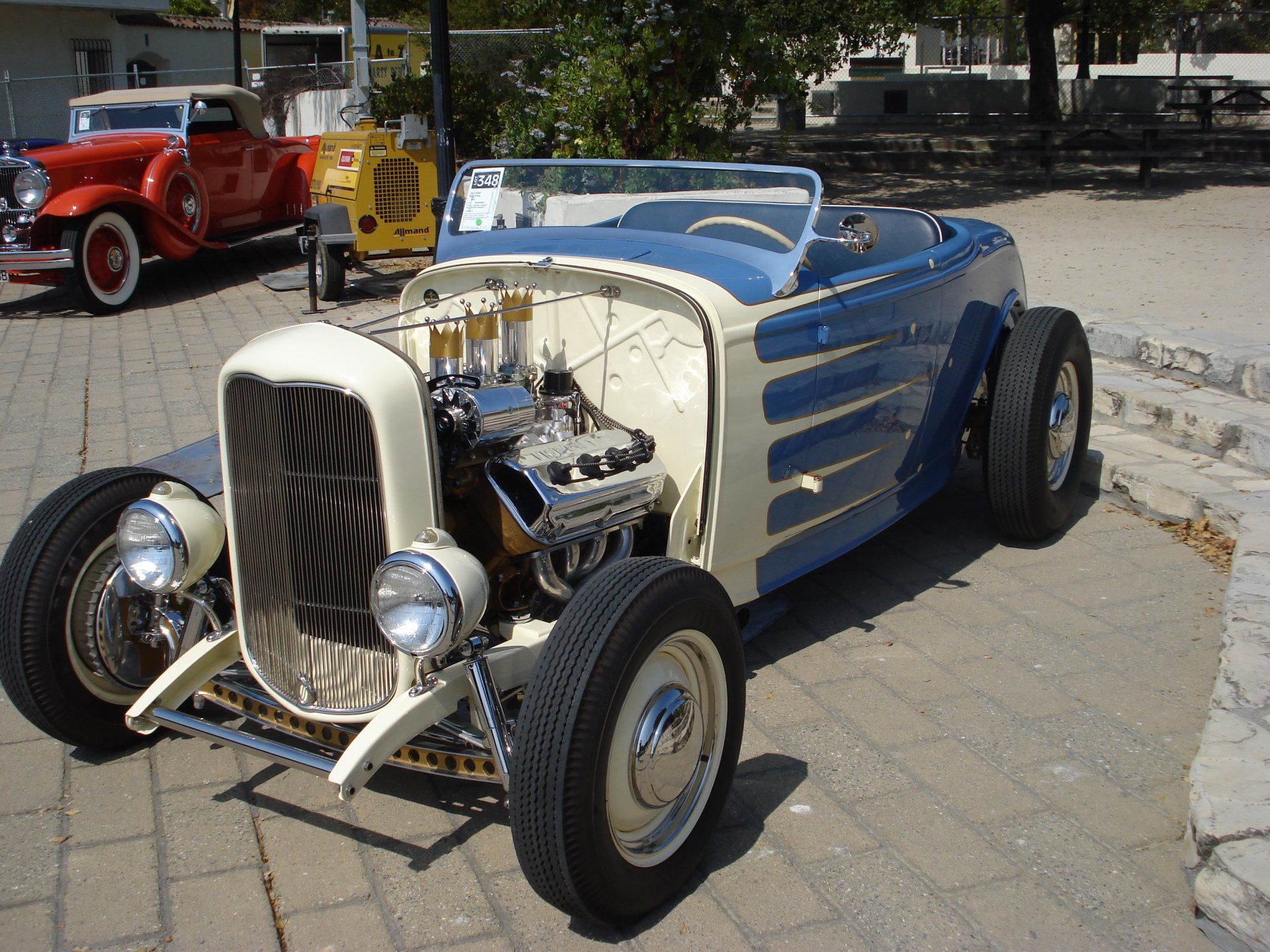 A blue and white hot rod is parked on a sidewalk