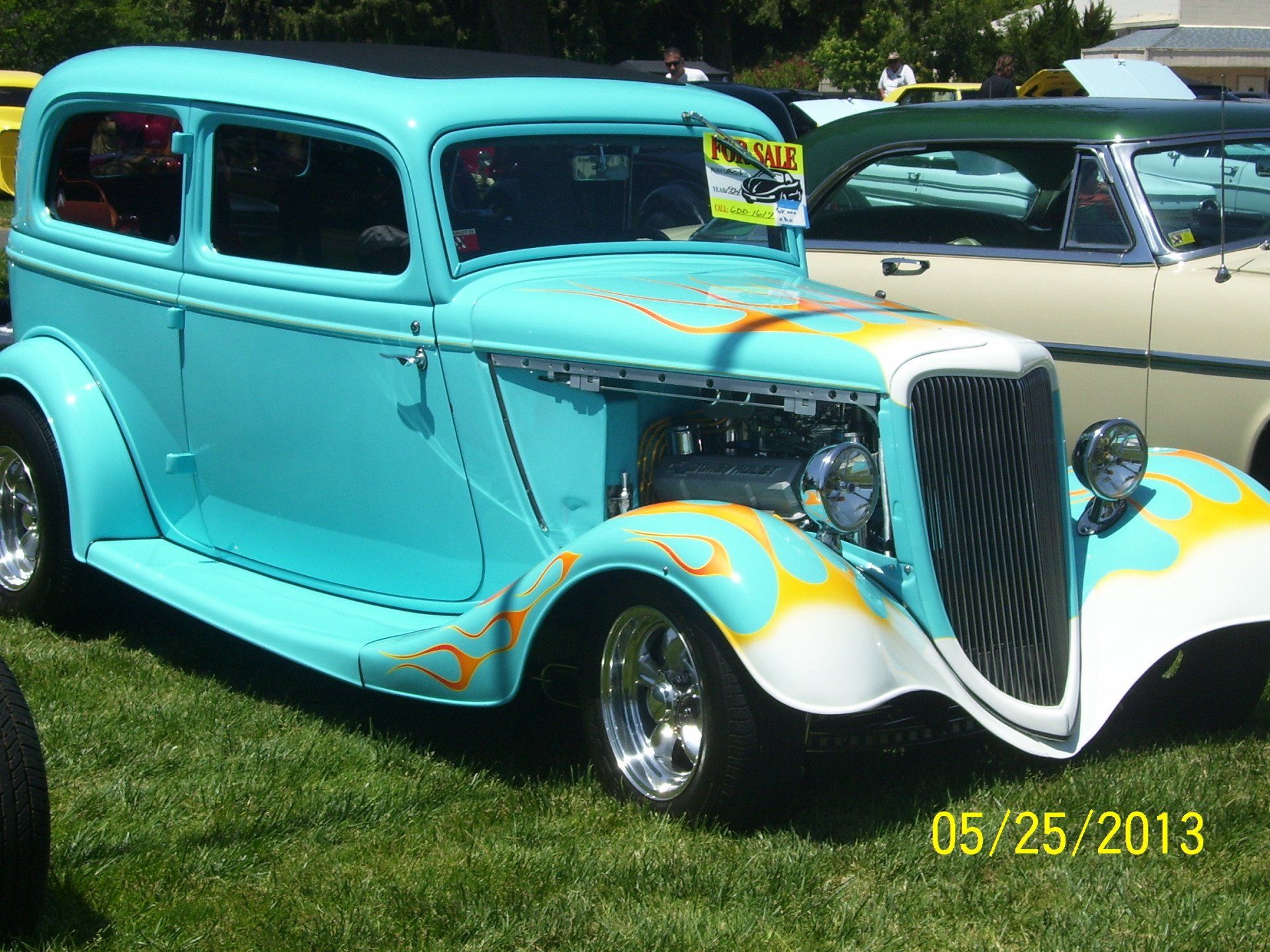 A blue car with flames painted on it is parked in the grass