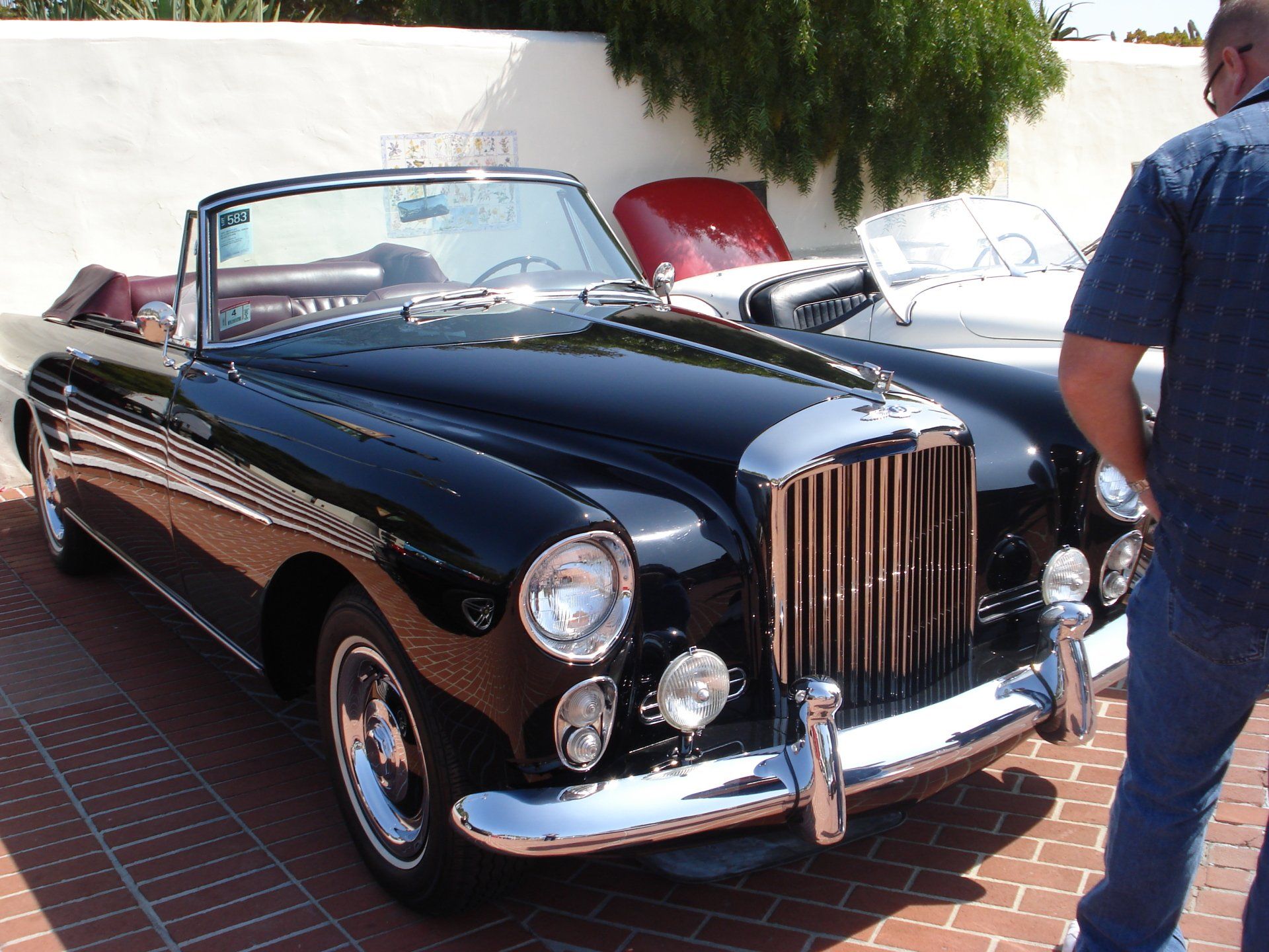 A man stands in front of a black rolls royce convertible