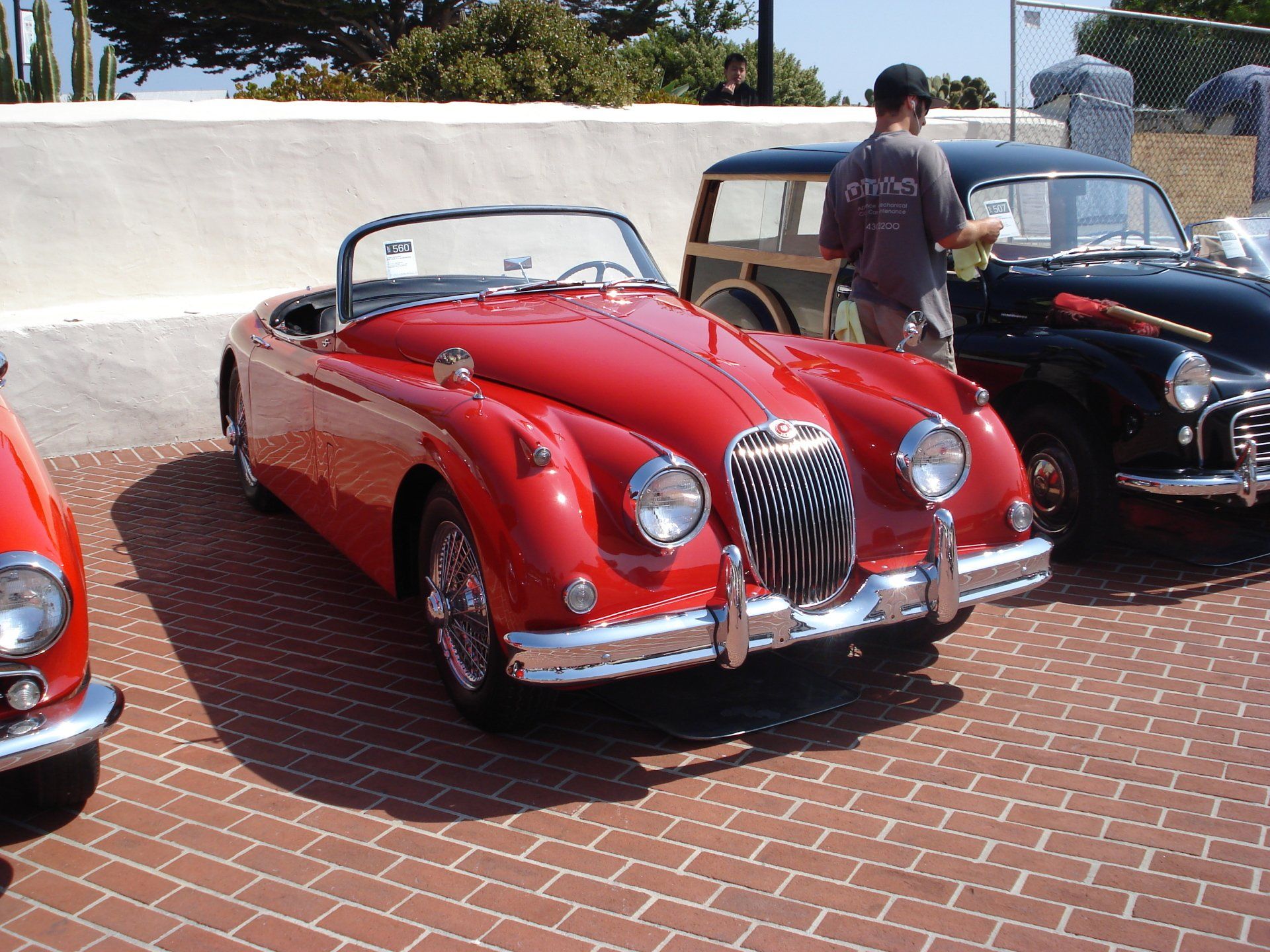 A red jaguar is parked next to a black car