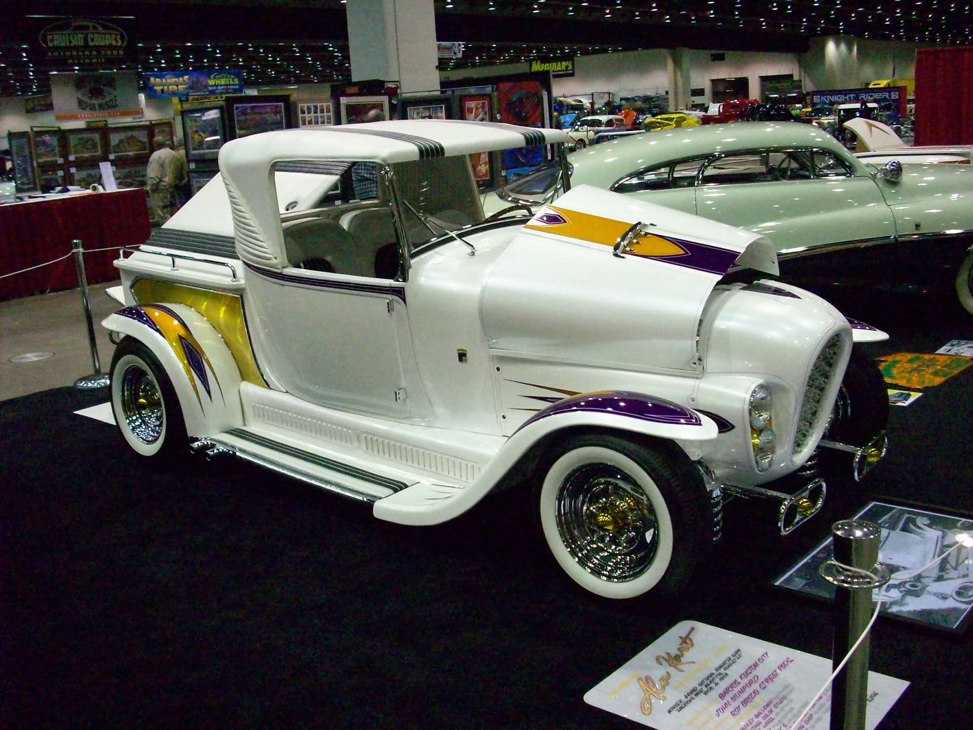 A white car with purple and yellow stripes is on display at a car show