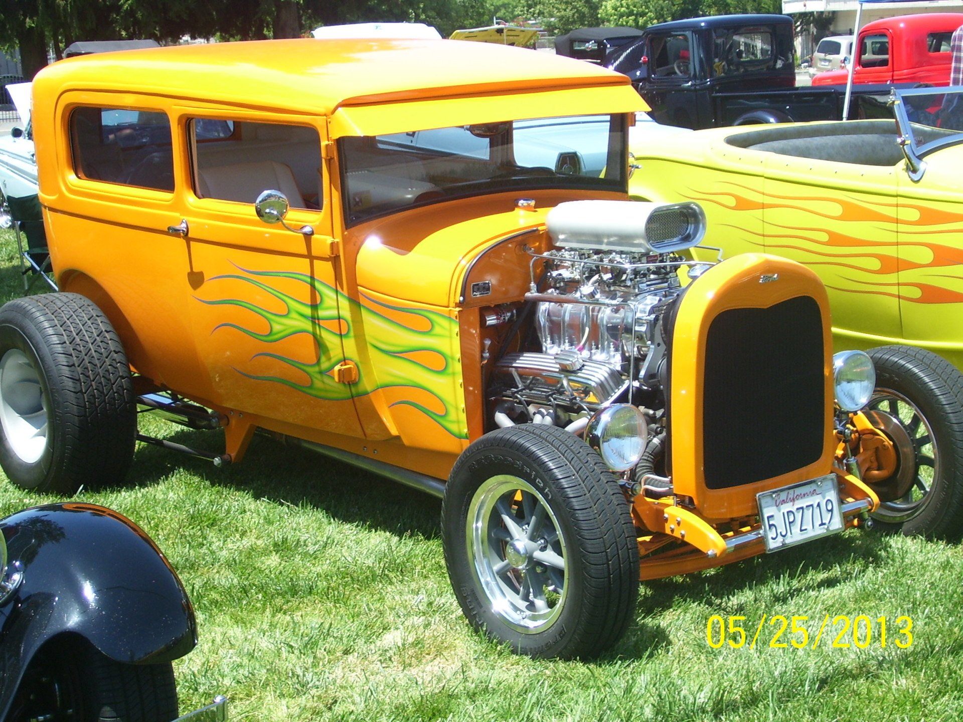 A yellow car with flames painted on it is parked in the grass