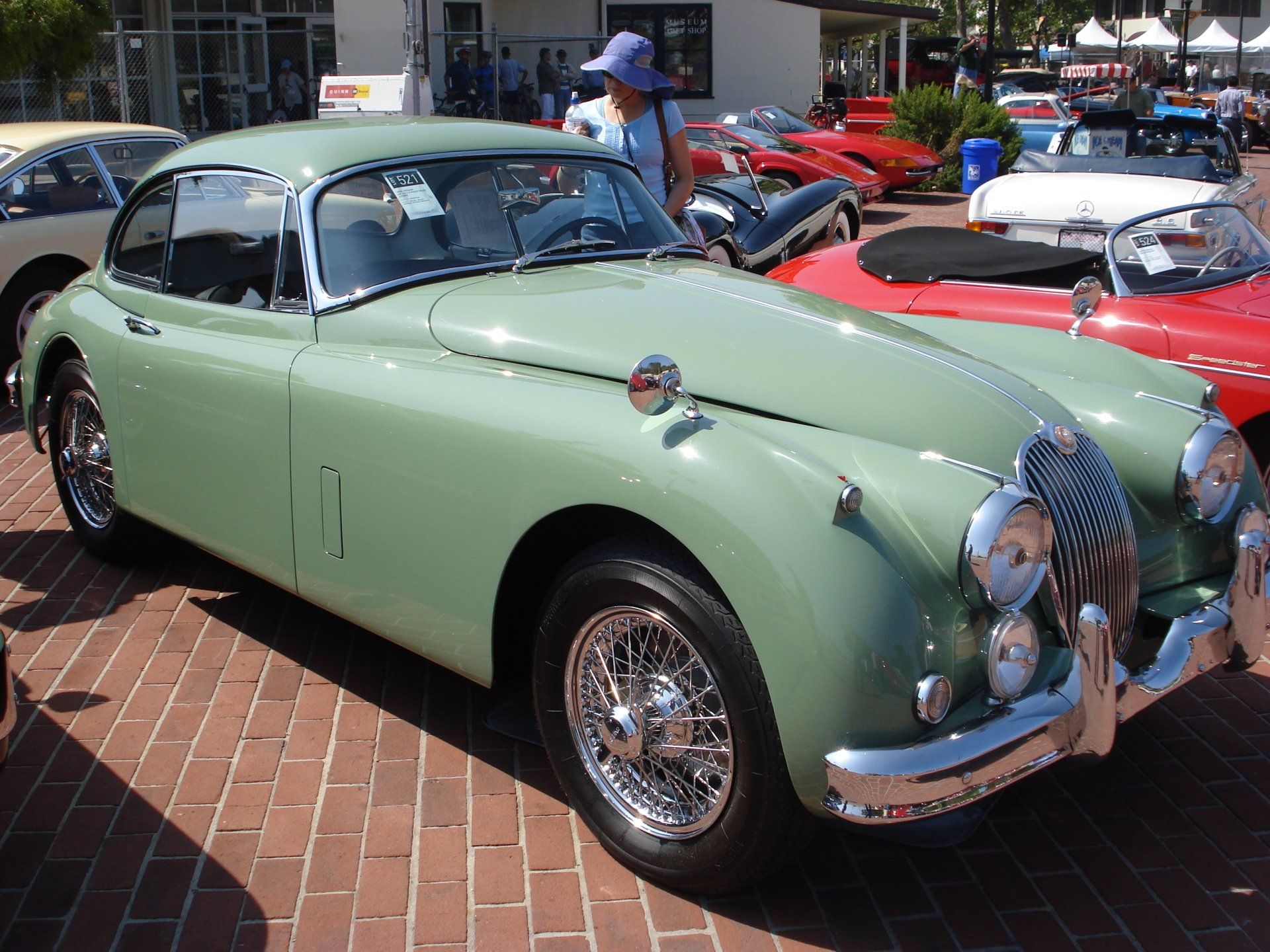 A green car is parked on a brick sidewalk