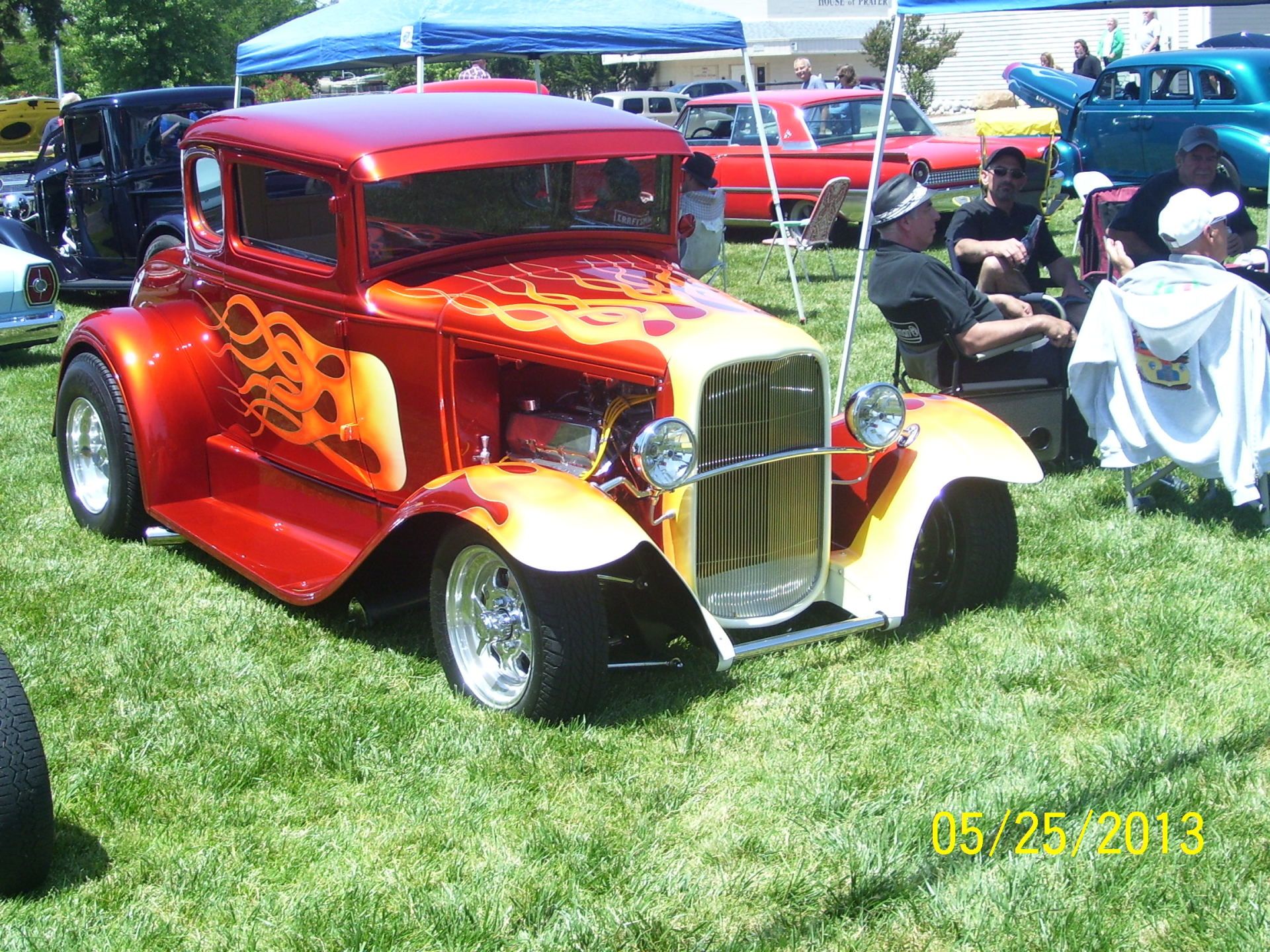 A red and yellow car is parked in the grass at a car show