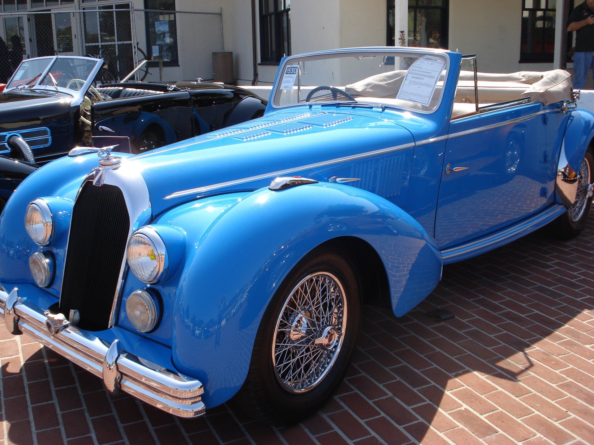 A blue car is parked on a brick sidewalk