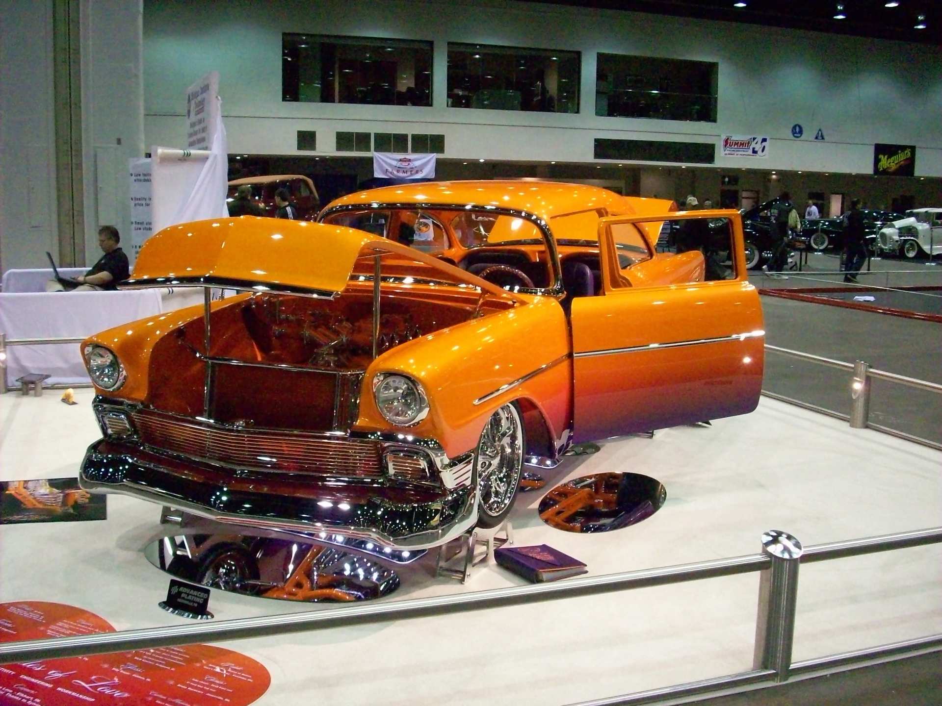 An orange car with the hood open is on display at a car show