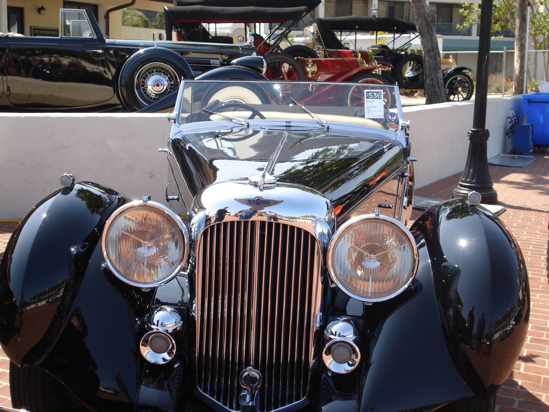 A black car with a clear windshield is parked on a brick sidewalk