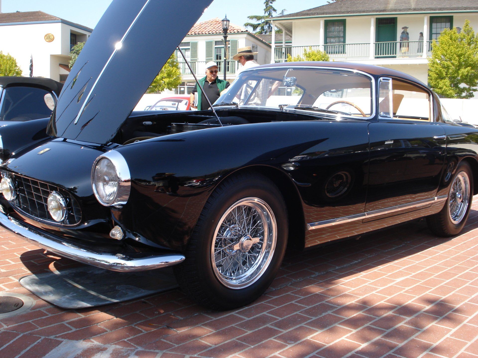 A black car with the hood up is parked on a brick driveway