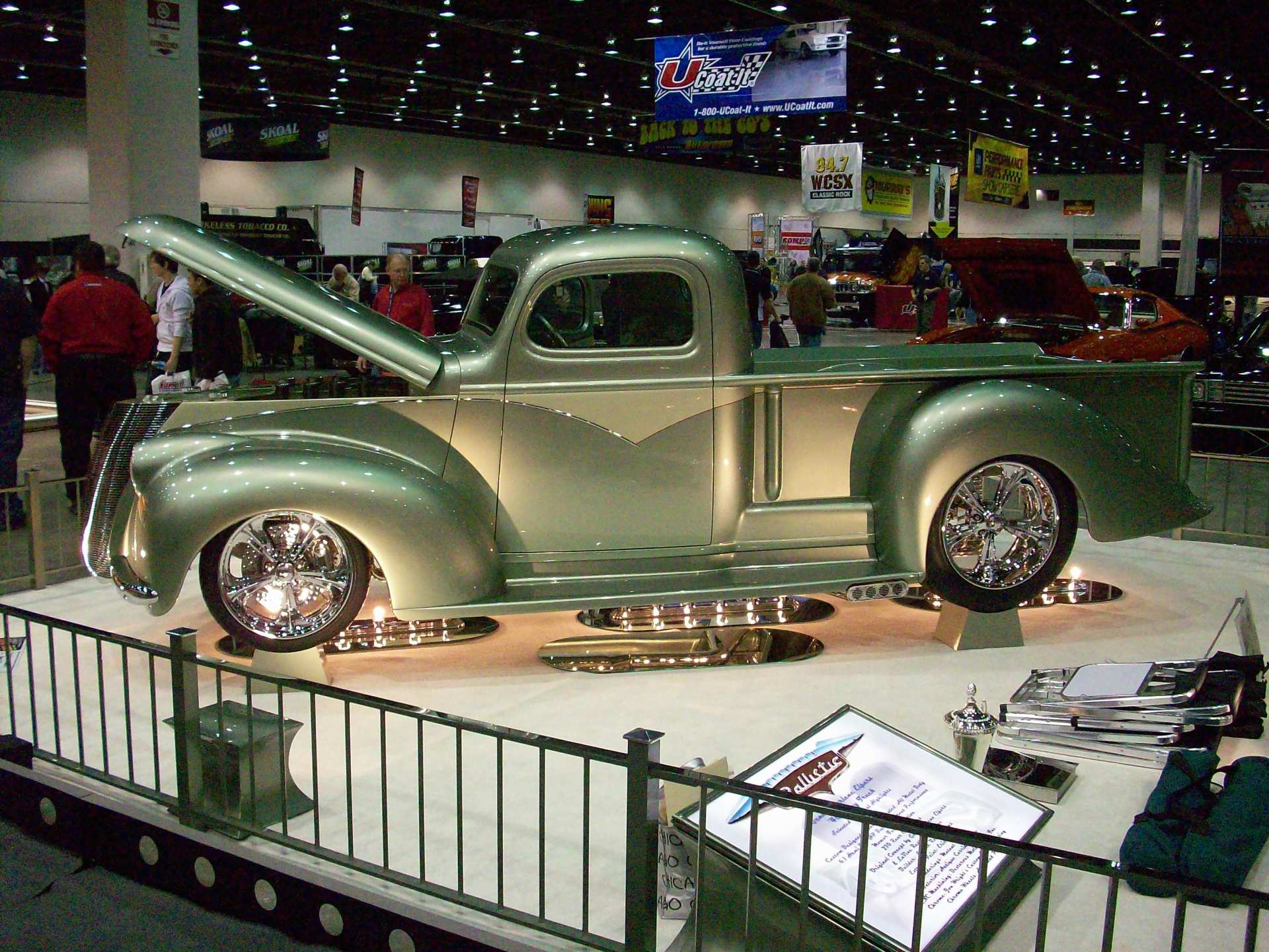 A silver truck with the hood up is on display at a car show