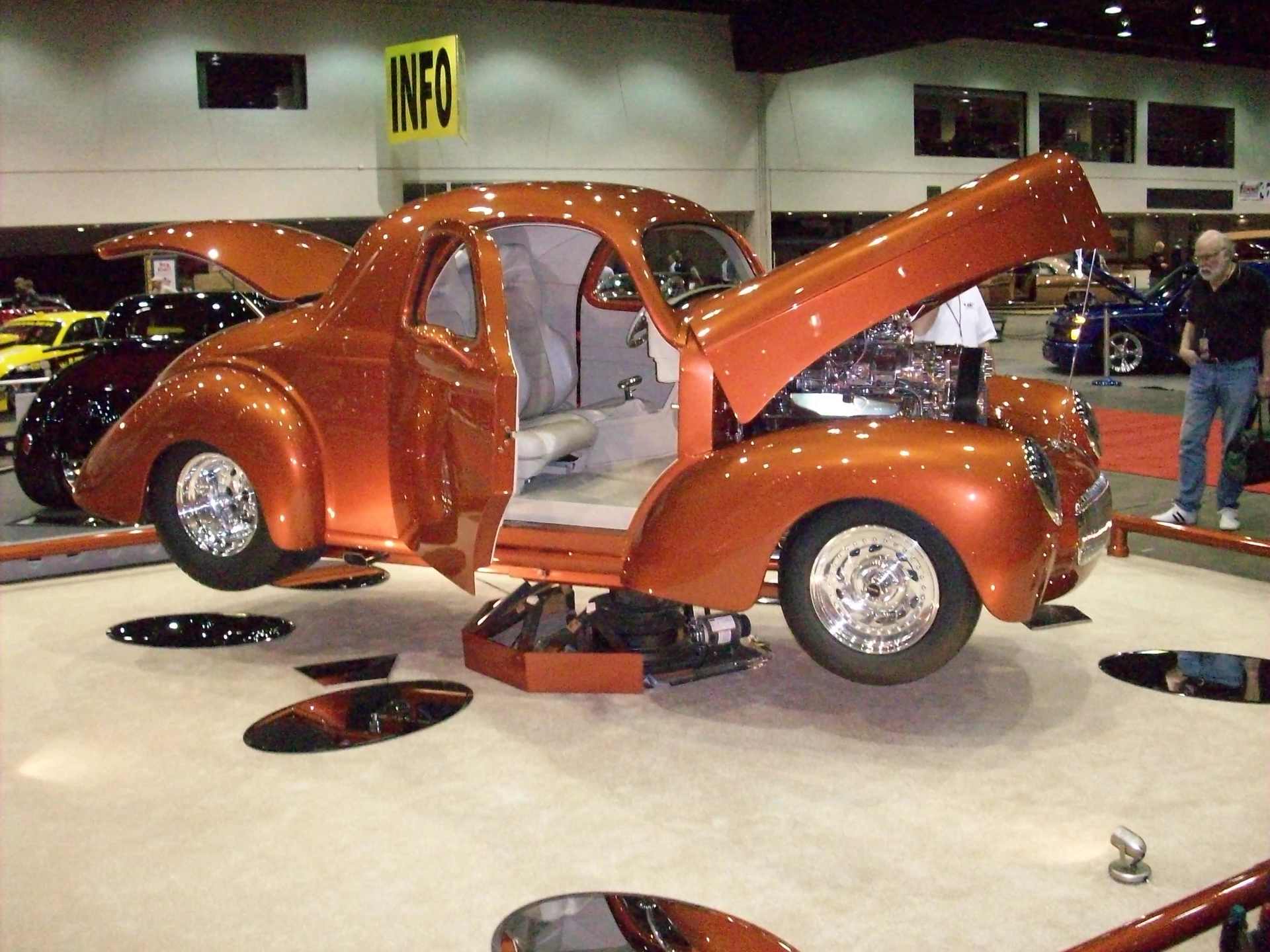 An orange car with the hood open is on display at a car show