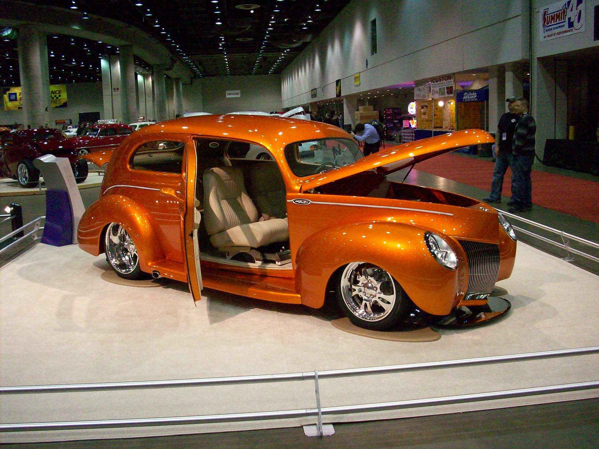 An orange car with the hood open is on display at a car show