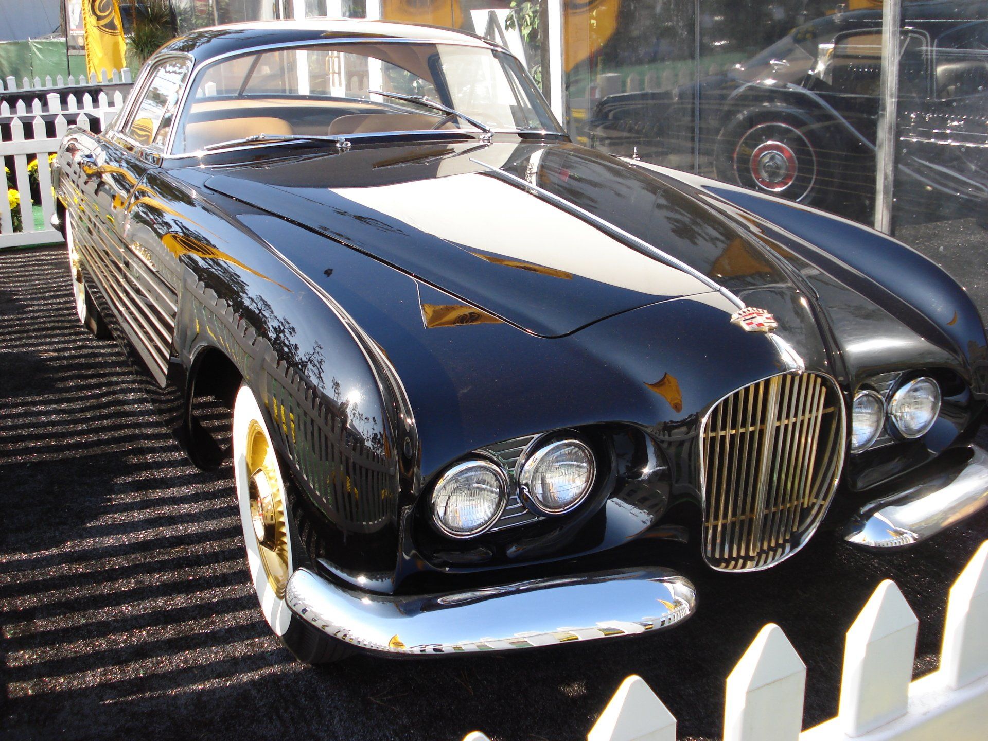 A black car is parked in front of a white picket fence