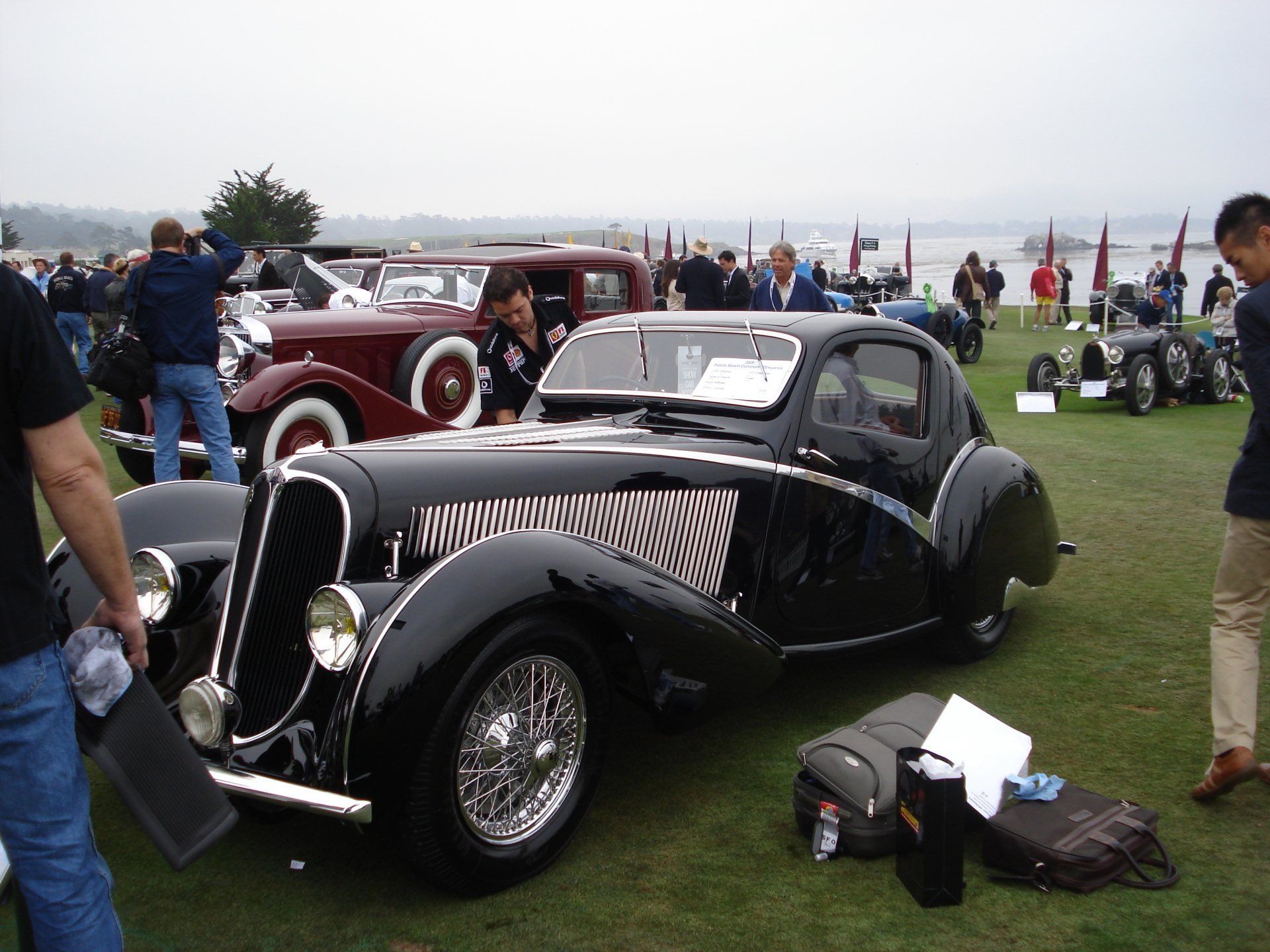 A black car is parked in a grassy field at a car show