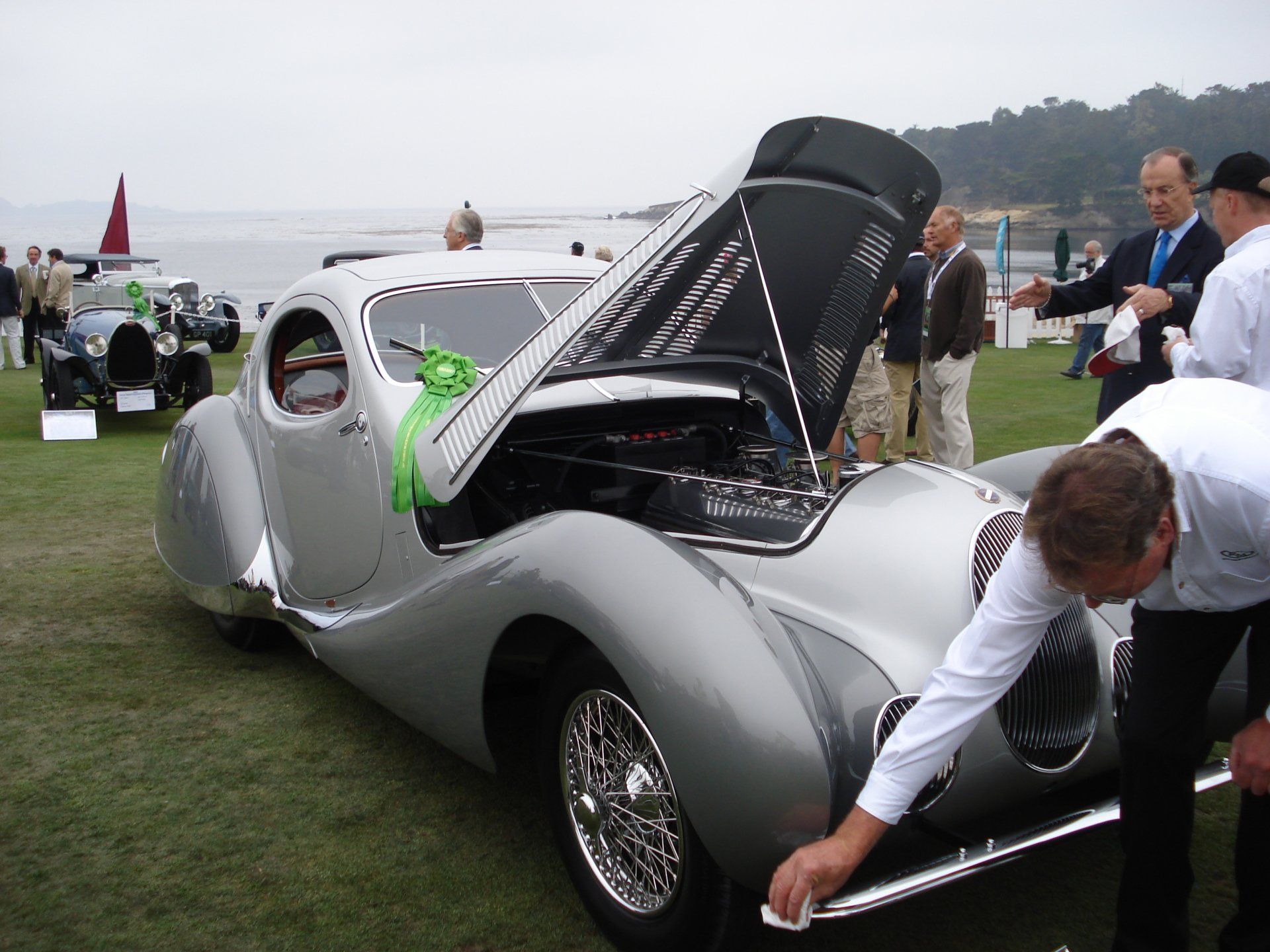A man cleaning a silver car with the hood open