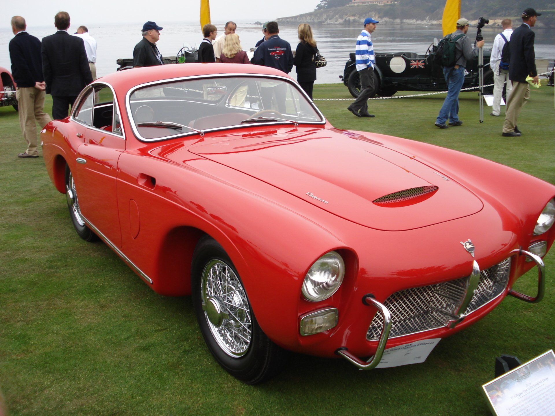 A group of people are standing around a red car