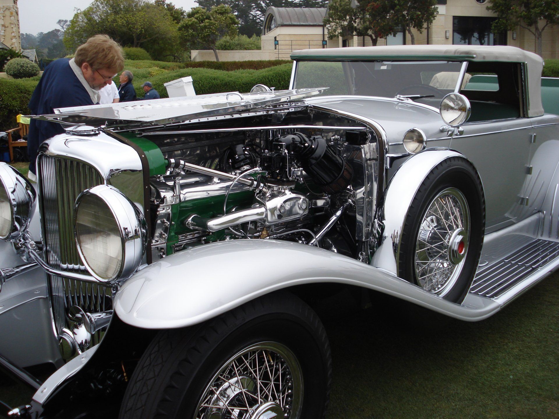 A man is looking under the hood of a silver car