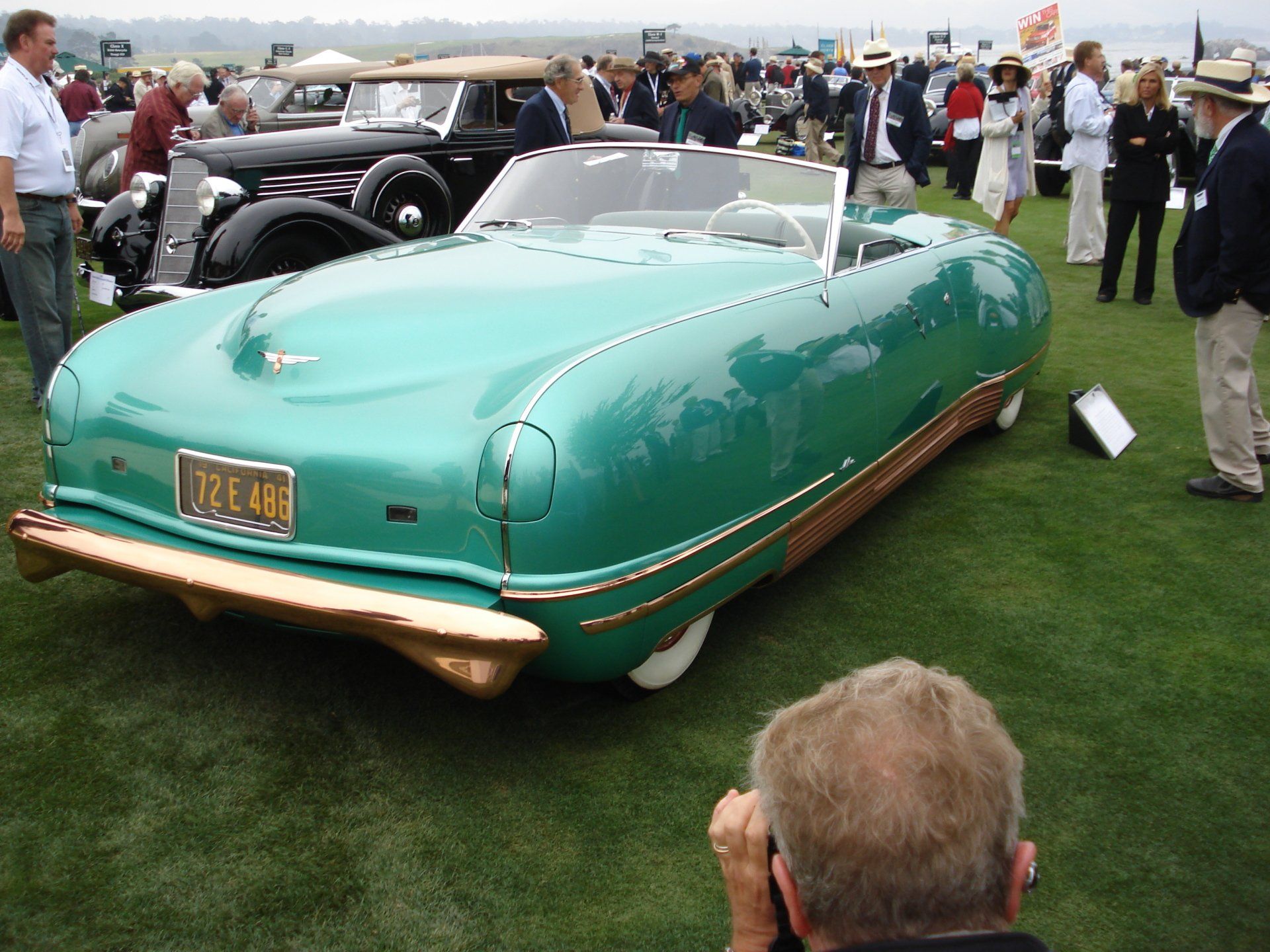 A man is taking a picture of a green car with a license plate that says ucl45