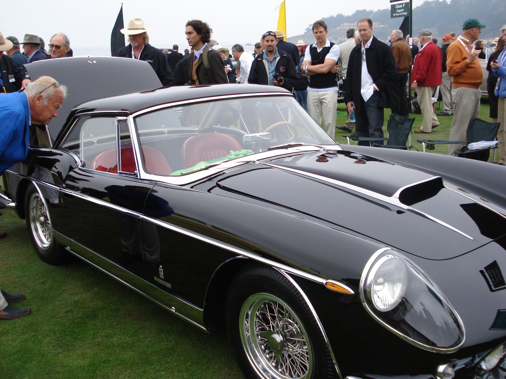 A group of people are gathered around a black sports car