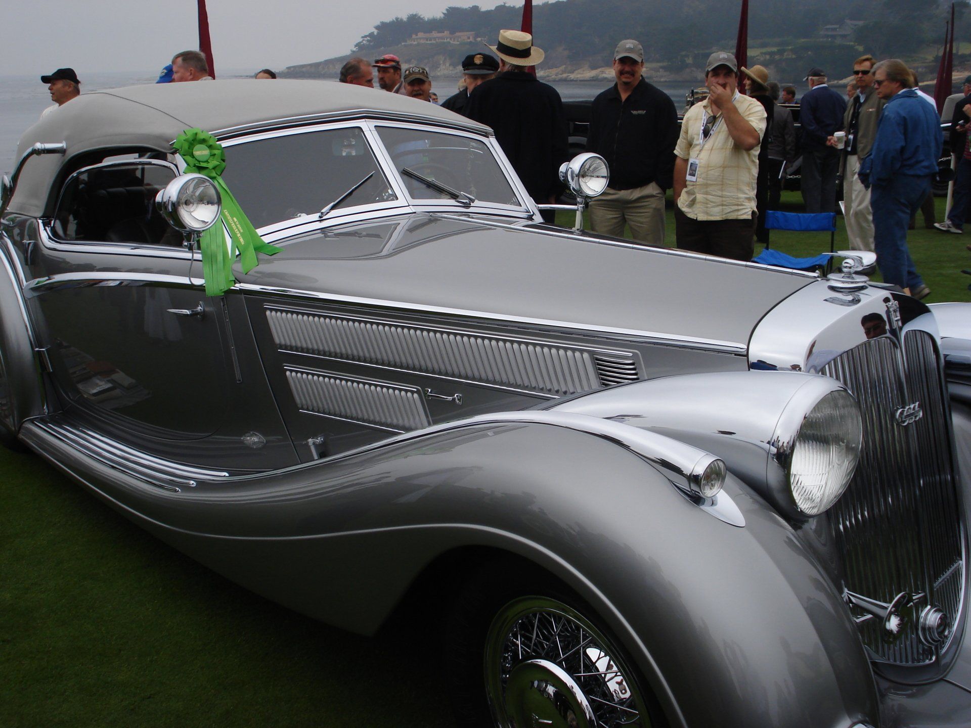 A silver car with a green ribbon on the windshield