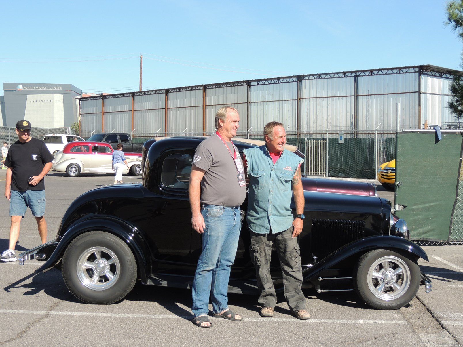 Two men are standing next to a black car in a parking lot.